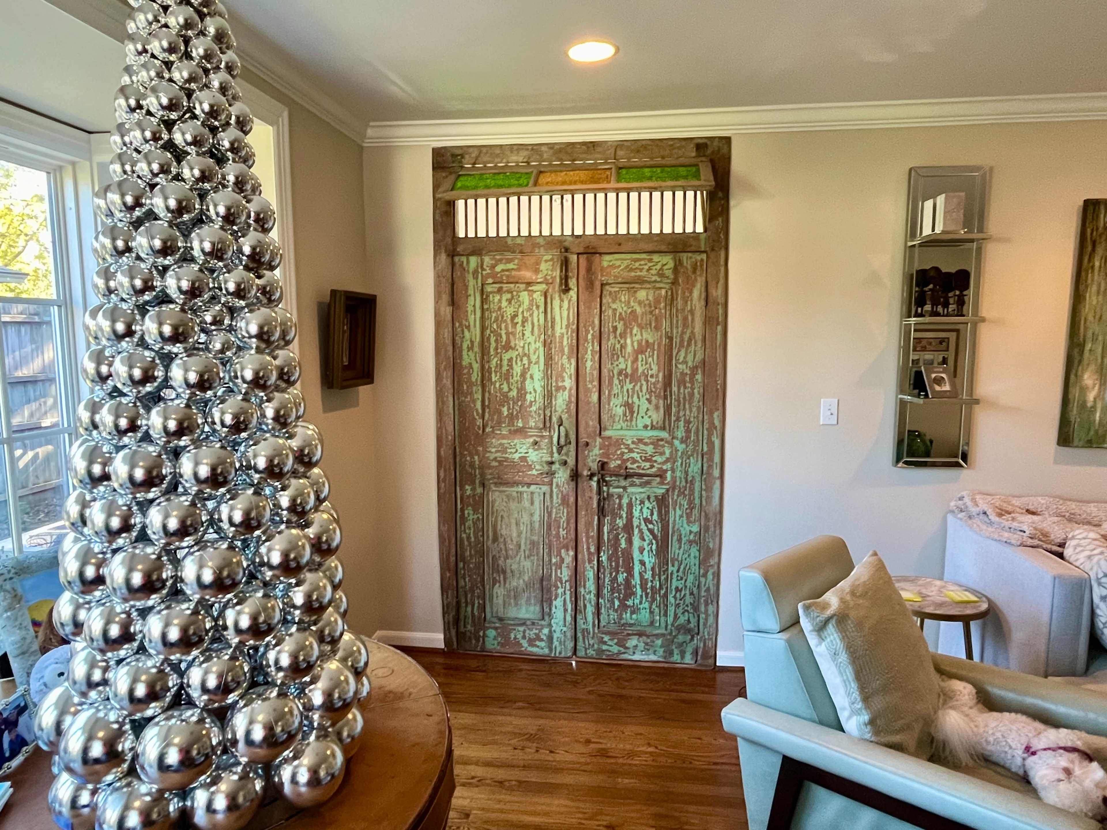 A decorated Christmas tree made of silver balls next to a pair of green wooden doors in a cozy room.