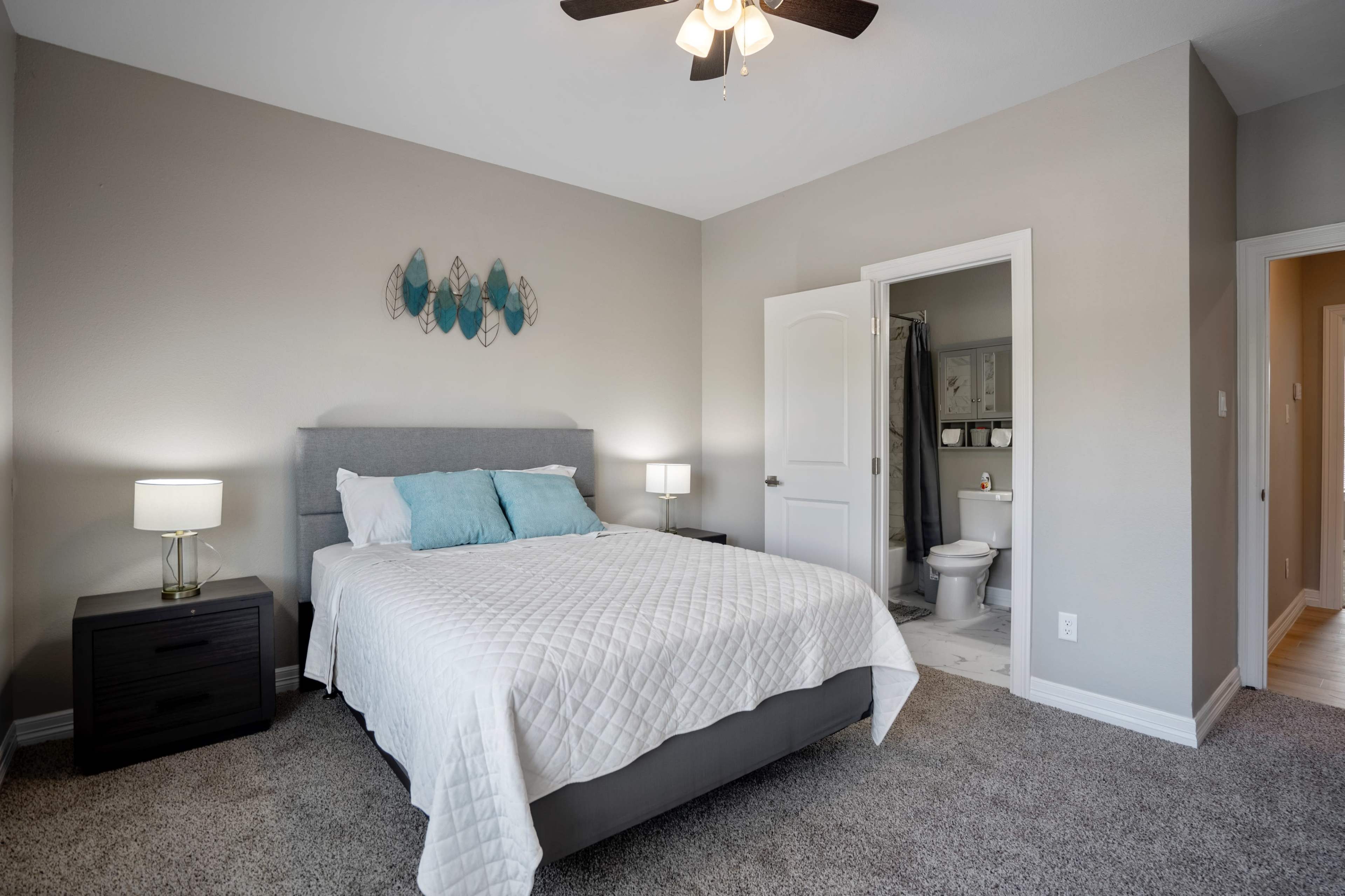 A neatly arranged bedroom with a bed, nightstands, and an open bathroom door in the background.