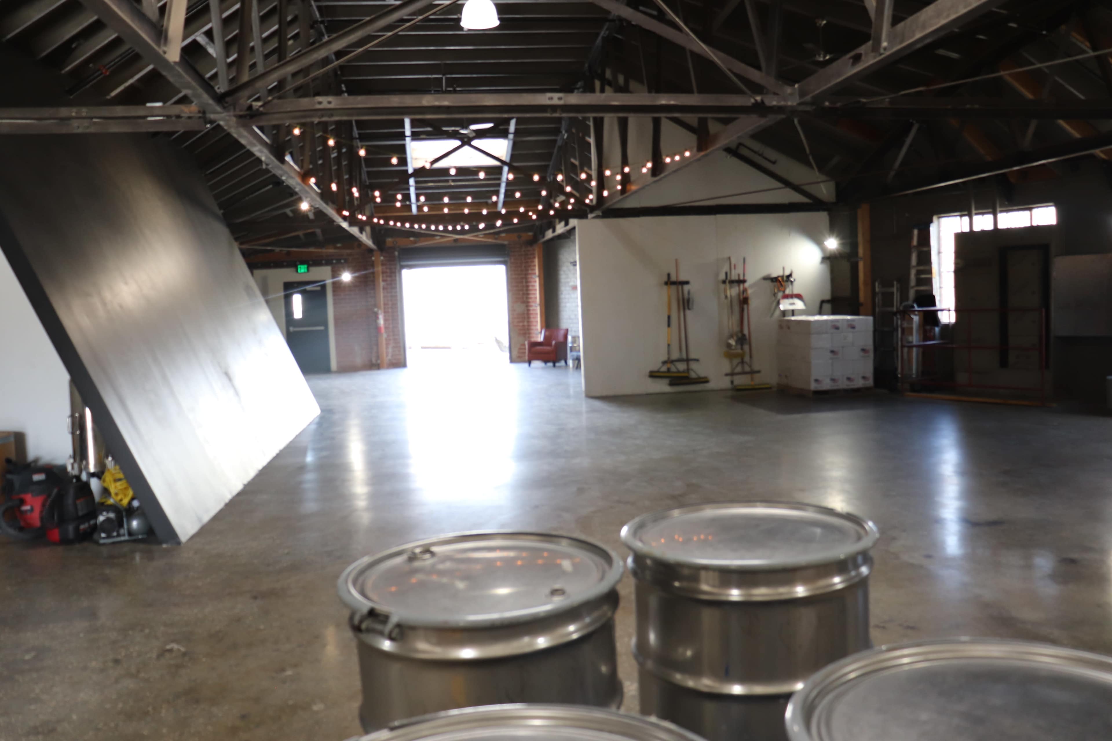 An industrial-style interior space with polished concrete floors, exposed beams, and several barrels in the foreground.