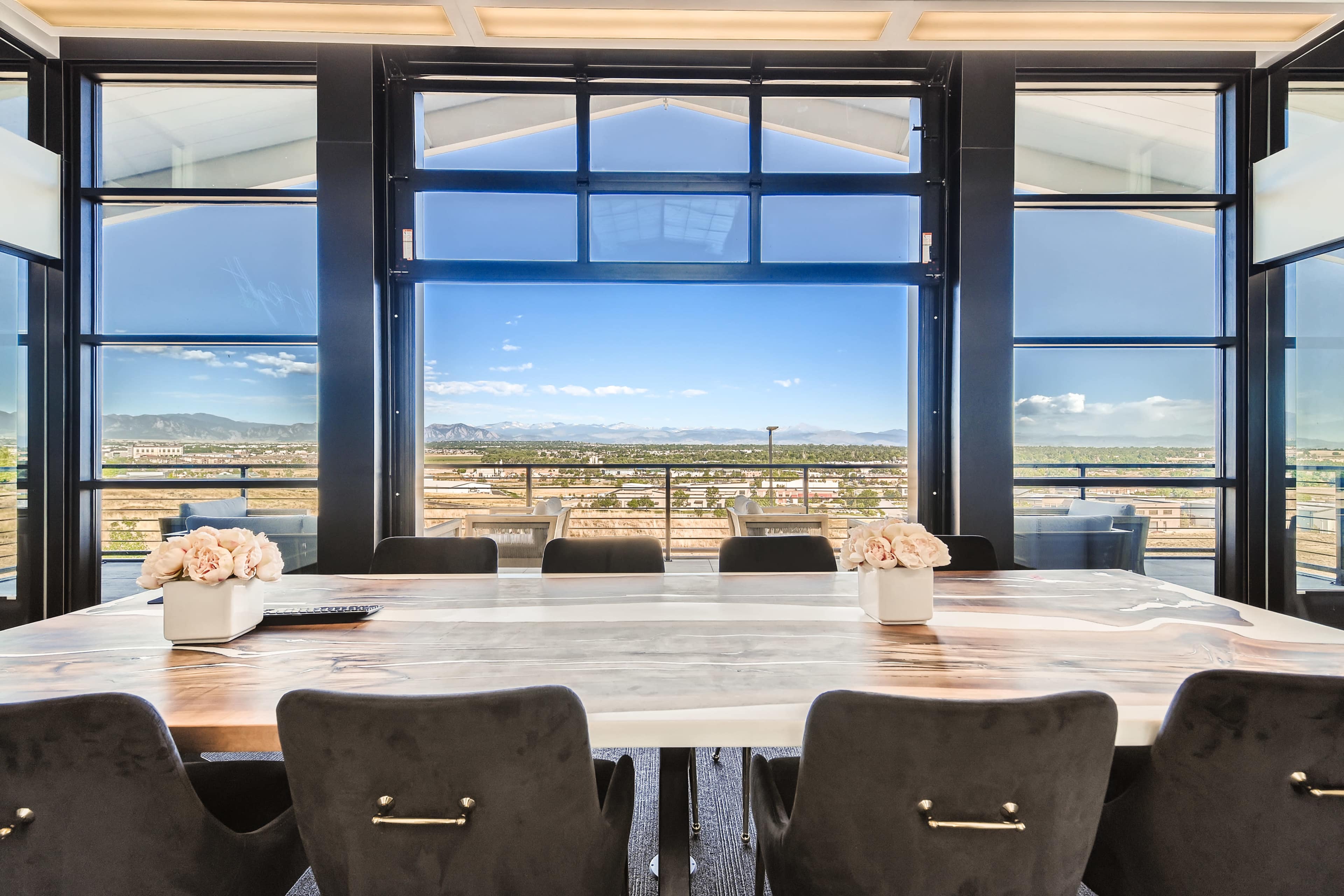 A large conference room features a long table with a view of mountains and cityscape through expansive windows.