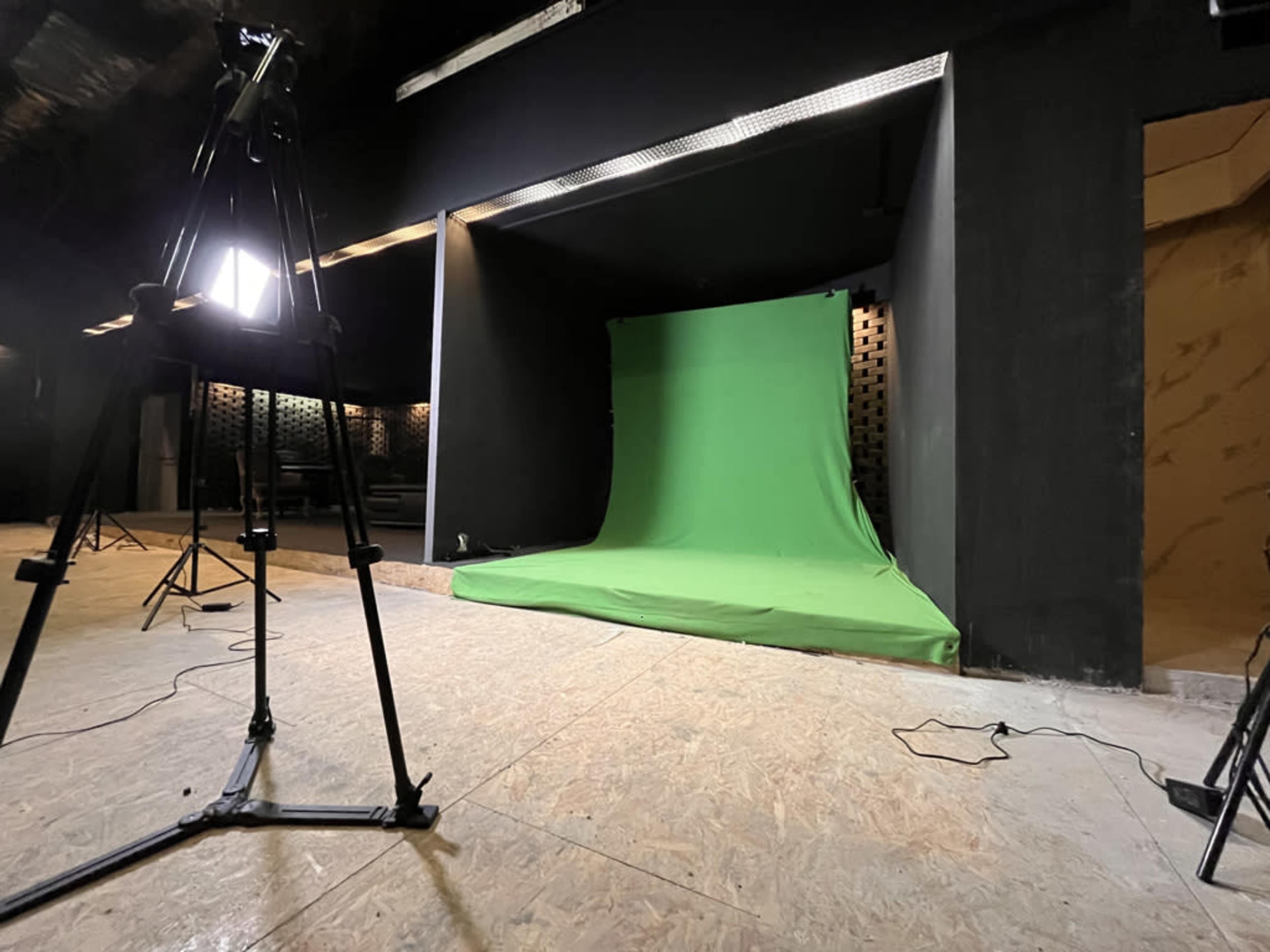 A photography studio features a green screen setup with lighting equipment positioned around the area.