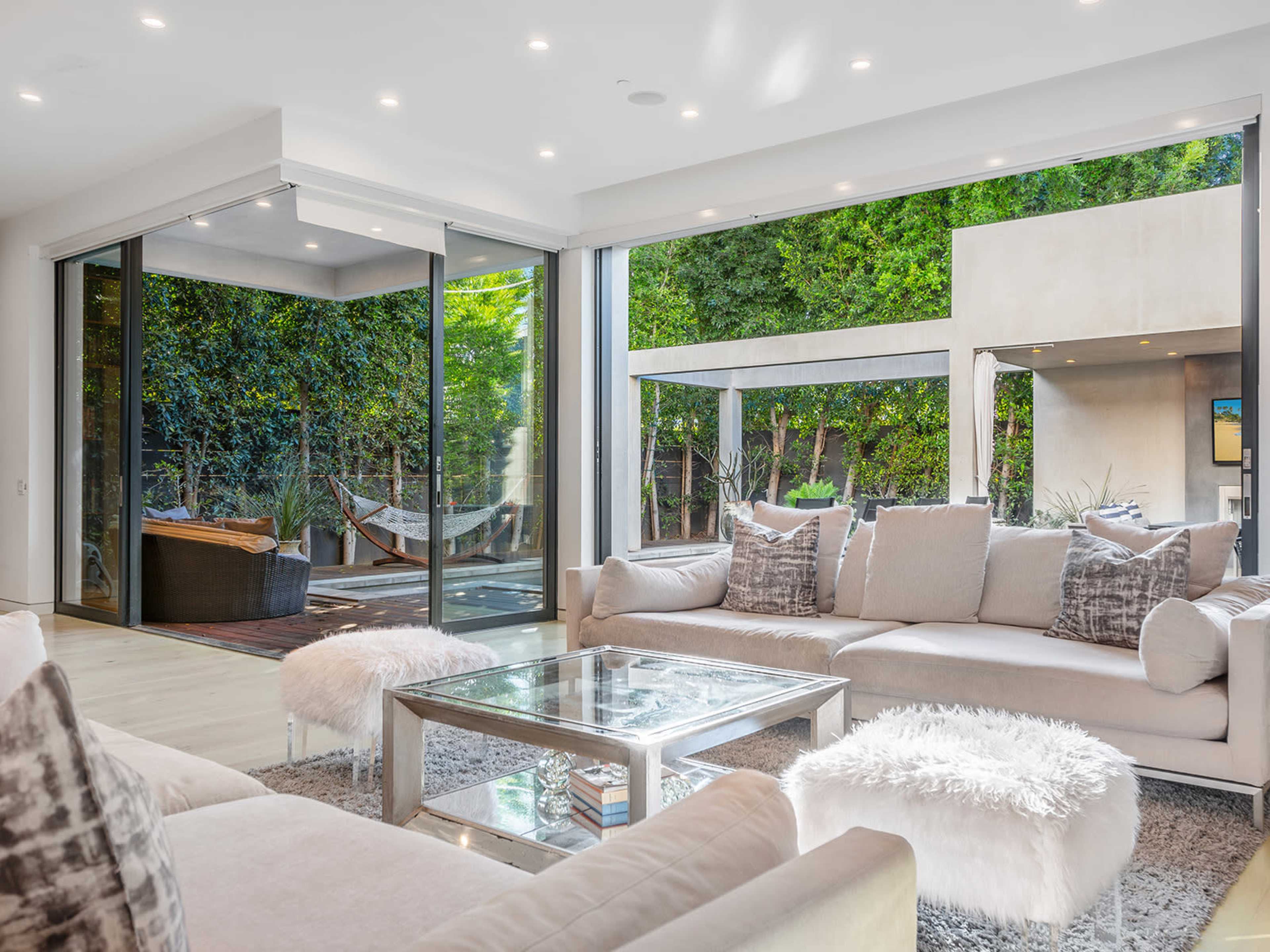A modern living room with a large glass door opening to an outdoor space featuring a hammock and greenery.