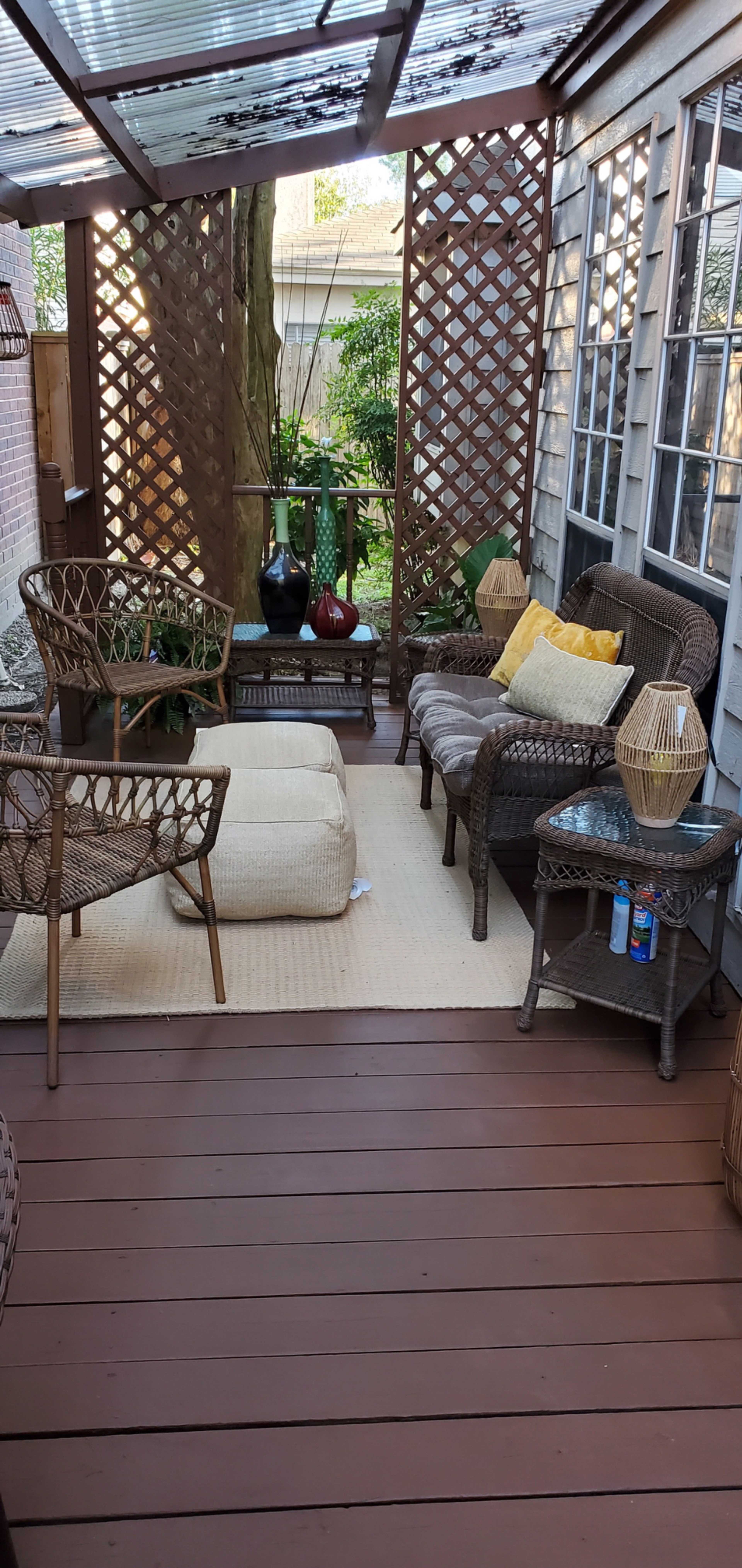 A cozy outdoor seating area features wicker furniture, a woven rug, and a lattice privacy screen amidst plants.