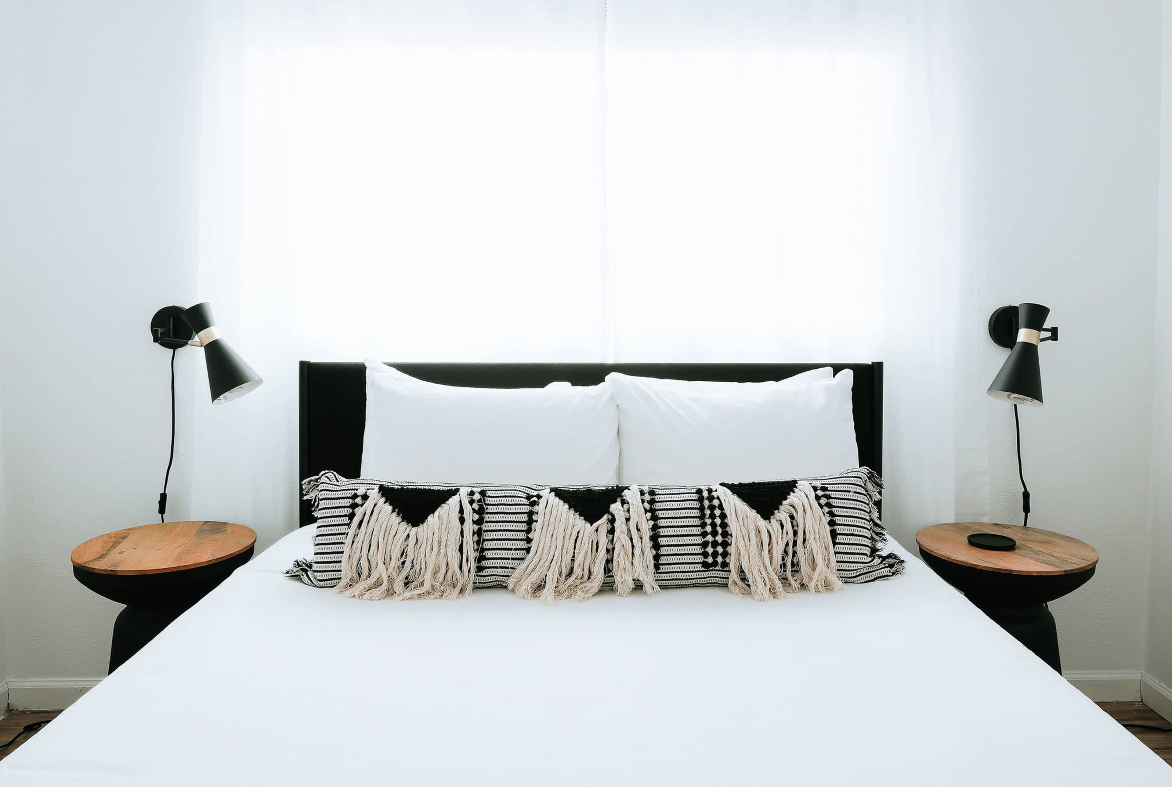 A neatly arranged bedroom features a black bed with white bedding, striped throw pillows, and two side tables with black lamps.