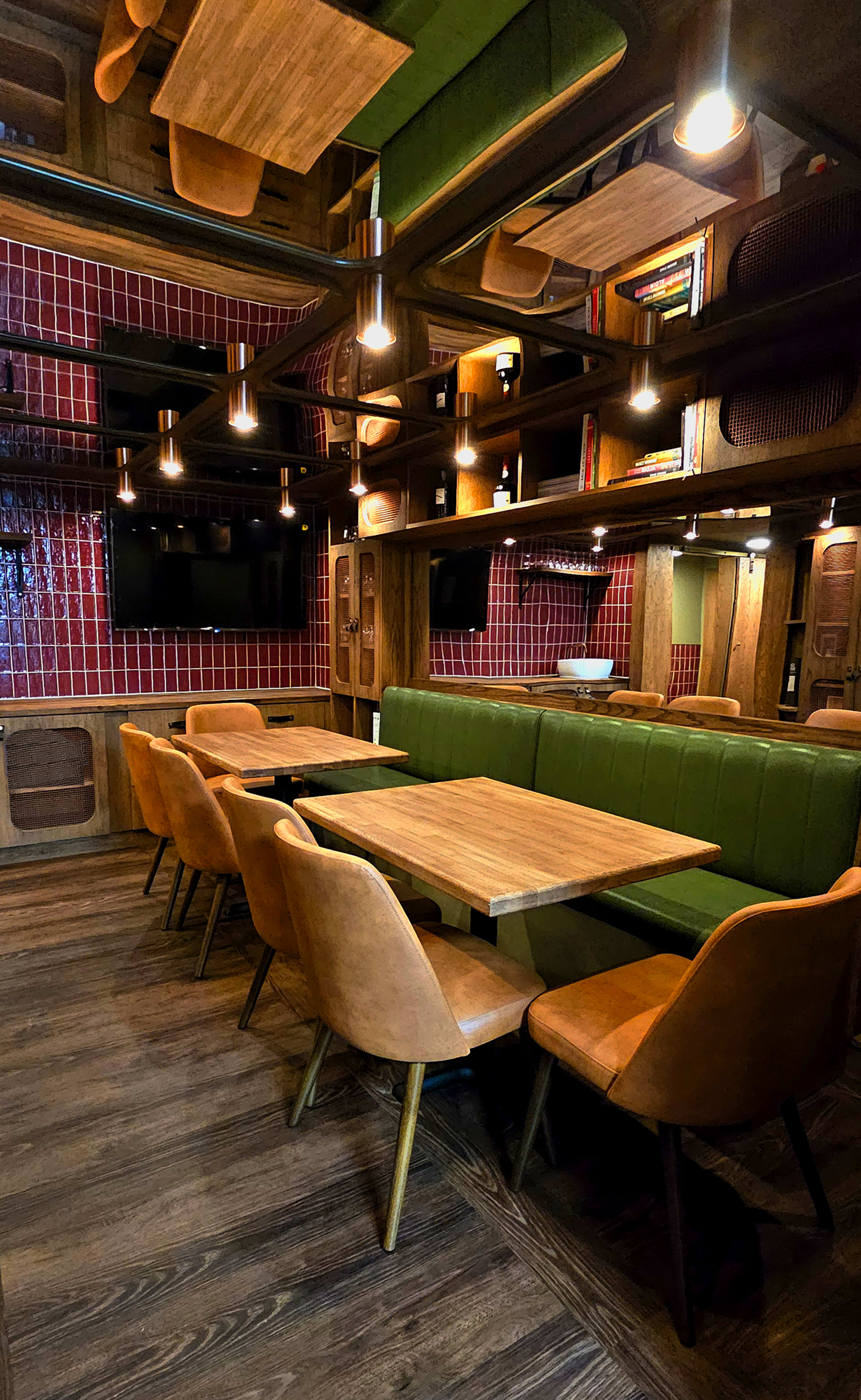 The image shows a modern restaurant interior featuring wooden tables and chairs, green booth seating, and decorative lighting on a red tiled wall.