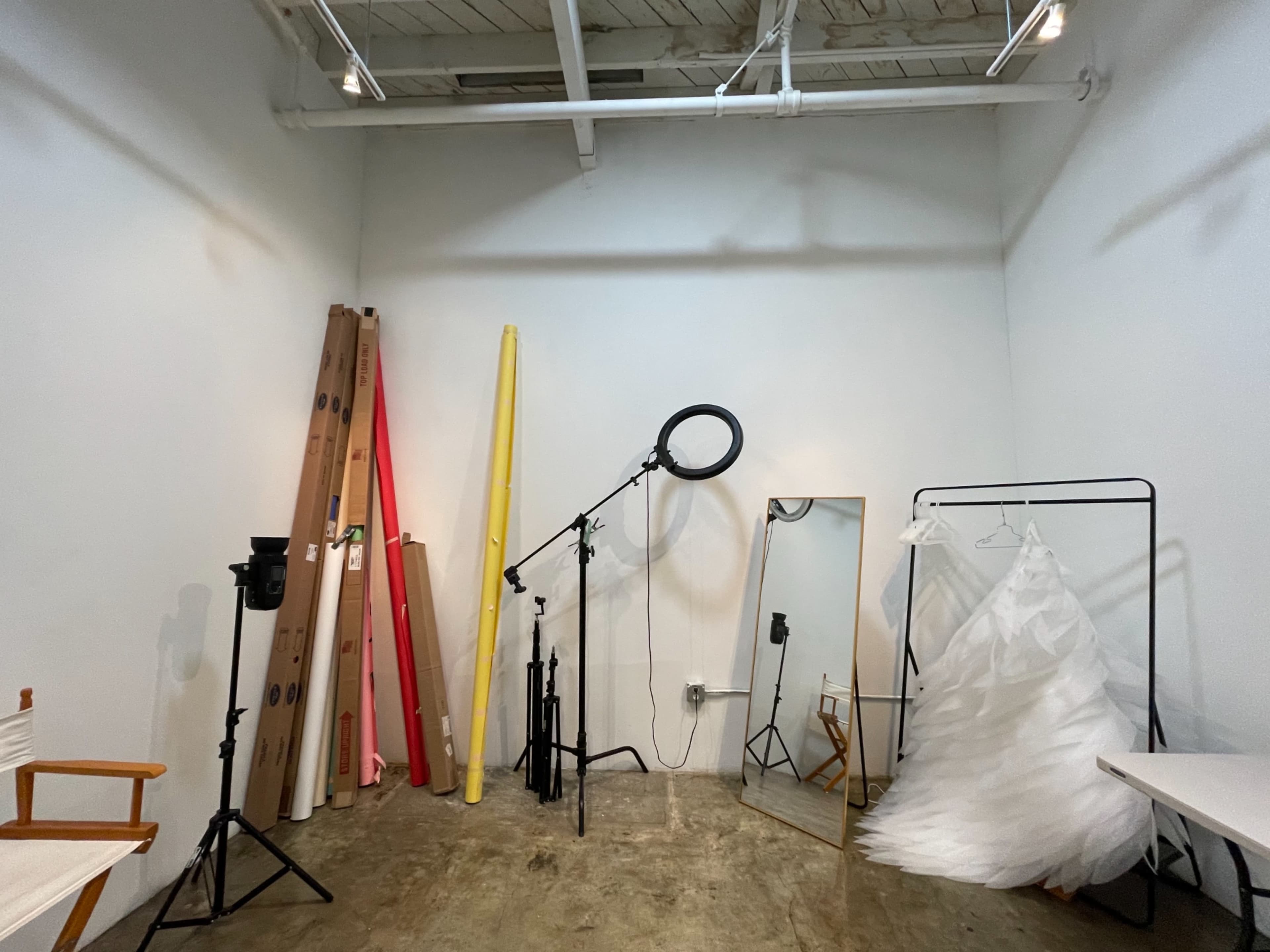 The image shows a photography studio with various props, including rolls of colored backdrops, lighting equipment, and a mirror.