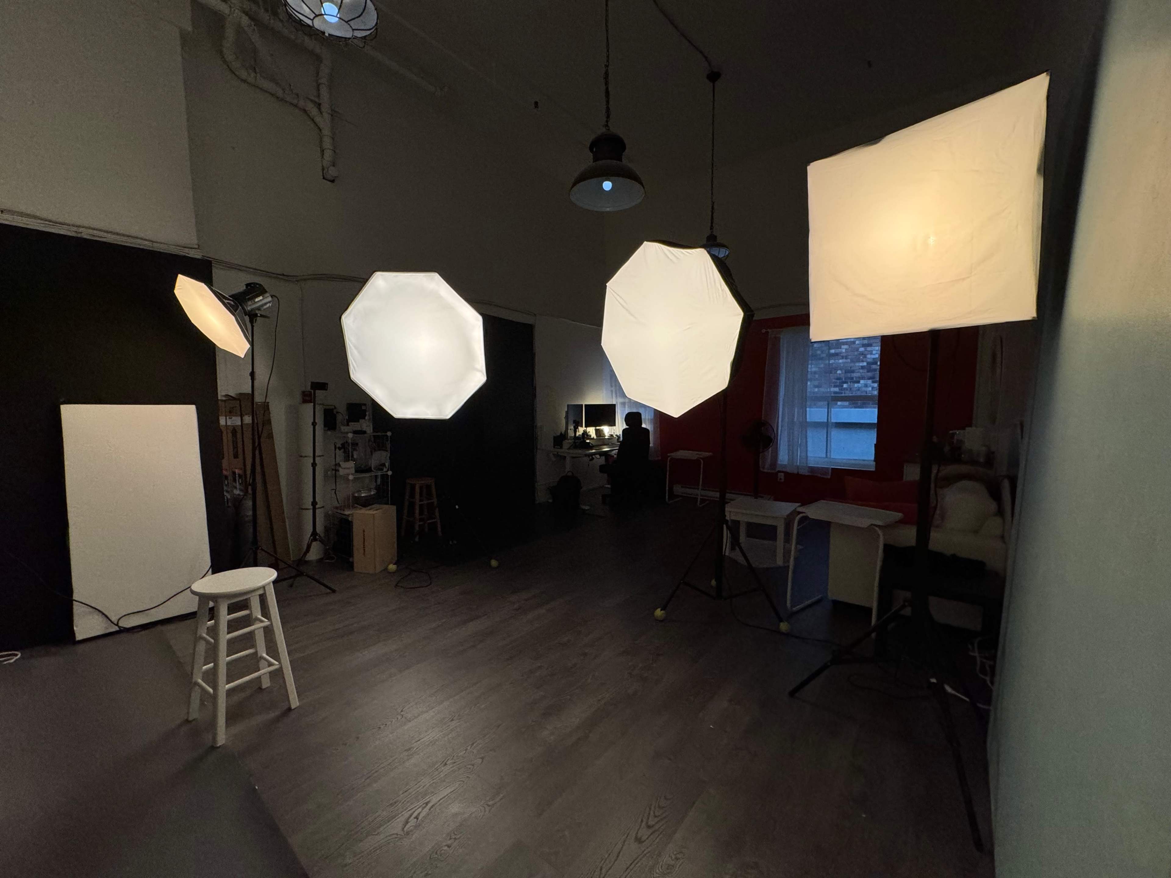 A photography studio with multiple softbox lights set up around a stool and a workspace in the background.