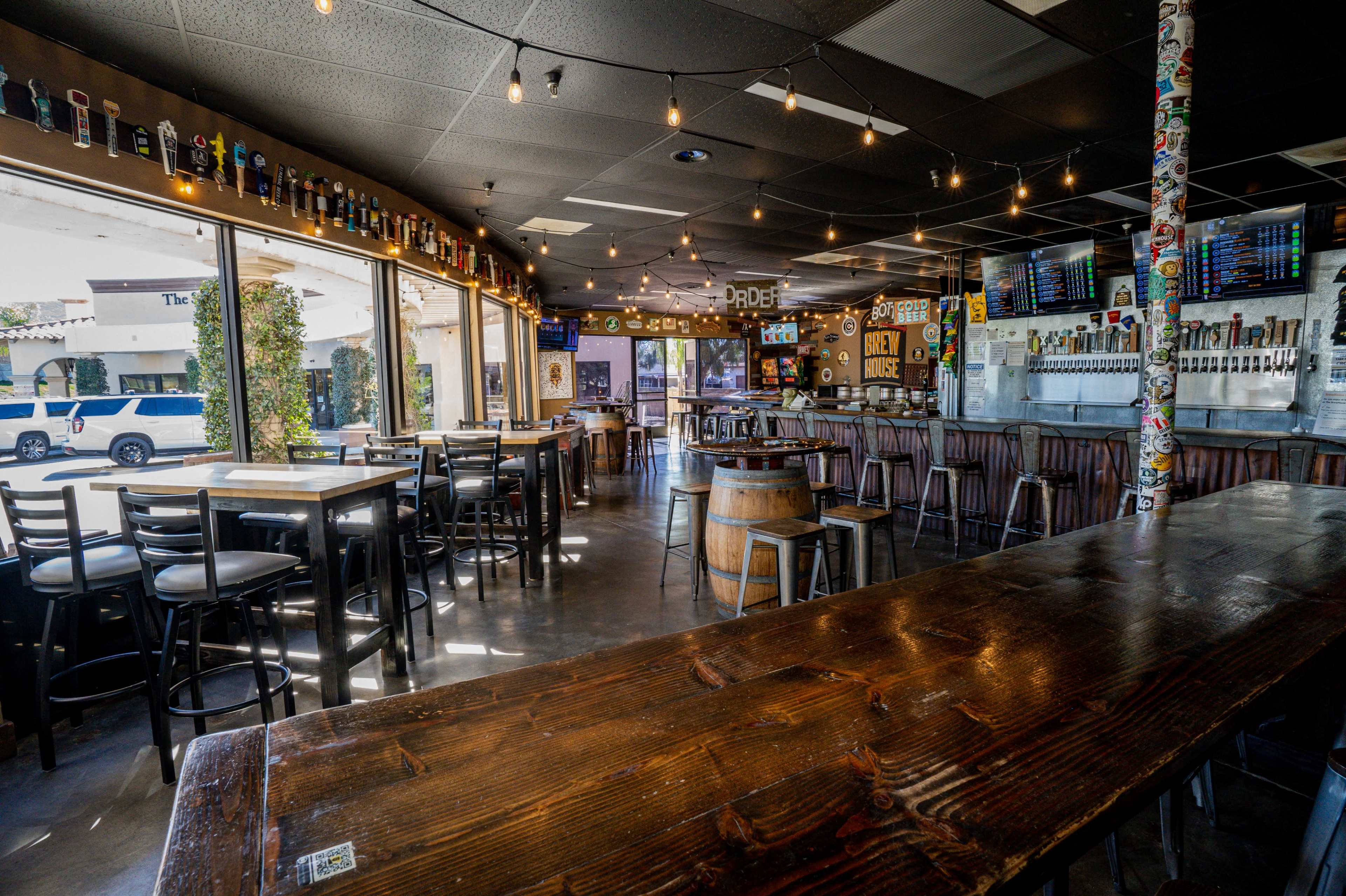 A casual bar with ample seating, large windows, and various beer taps displayed behind the counter.