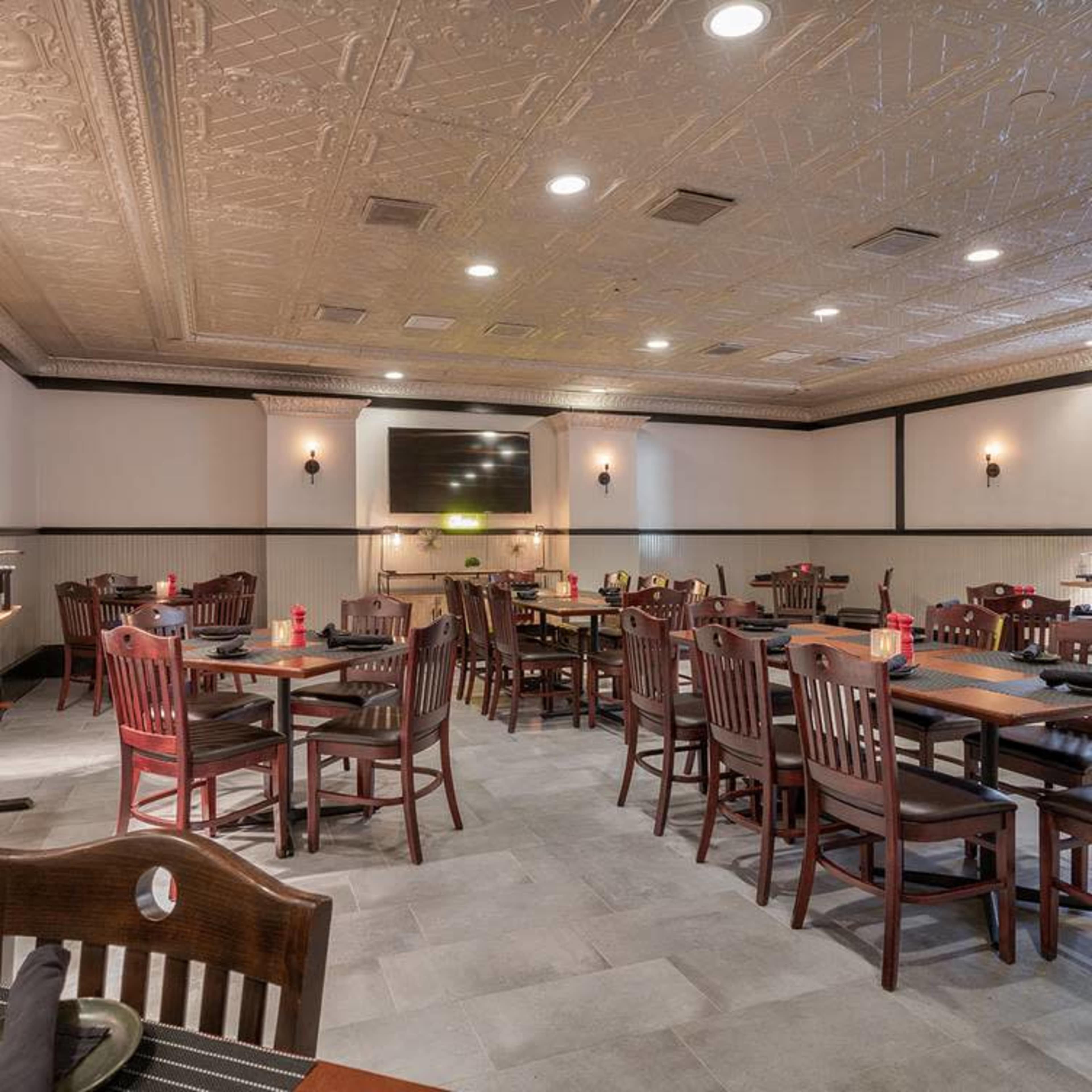 A spacious restaurant interior with wooden tables and chairs, a tiled floor, and decorative ceiling tiles.