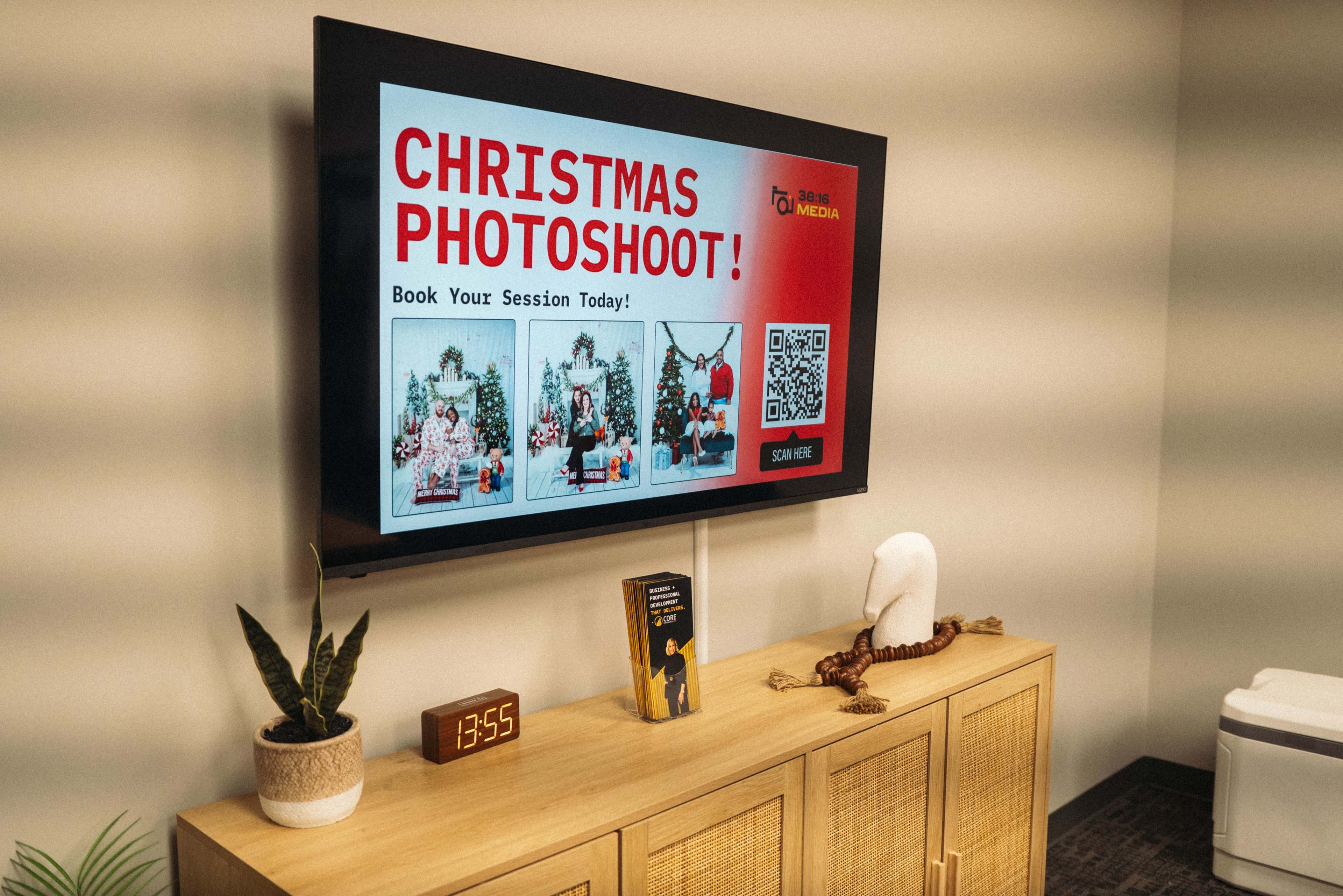 The image shows a television displaying a promotional advertisement for a Christmas photoshoot, featuring booking details alongside holiday-themed decorations.
