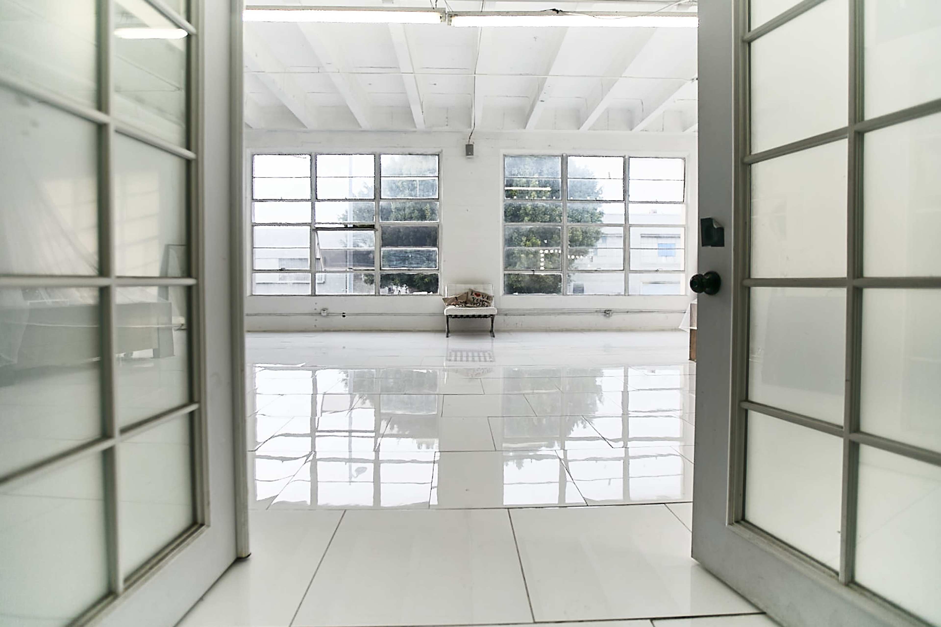 The image shows an open entrance leading into a bright, spacious room with glossy tiled floors and large windows that allow natural light to flood in.