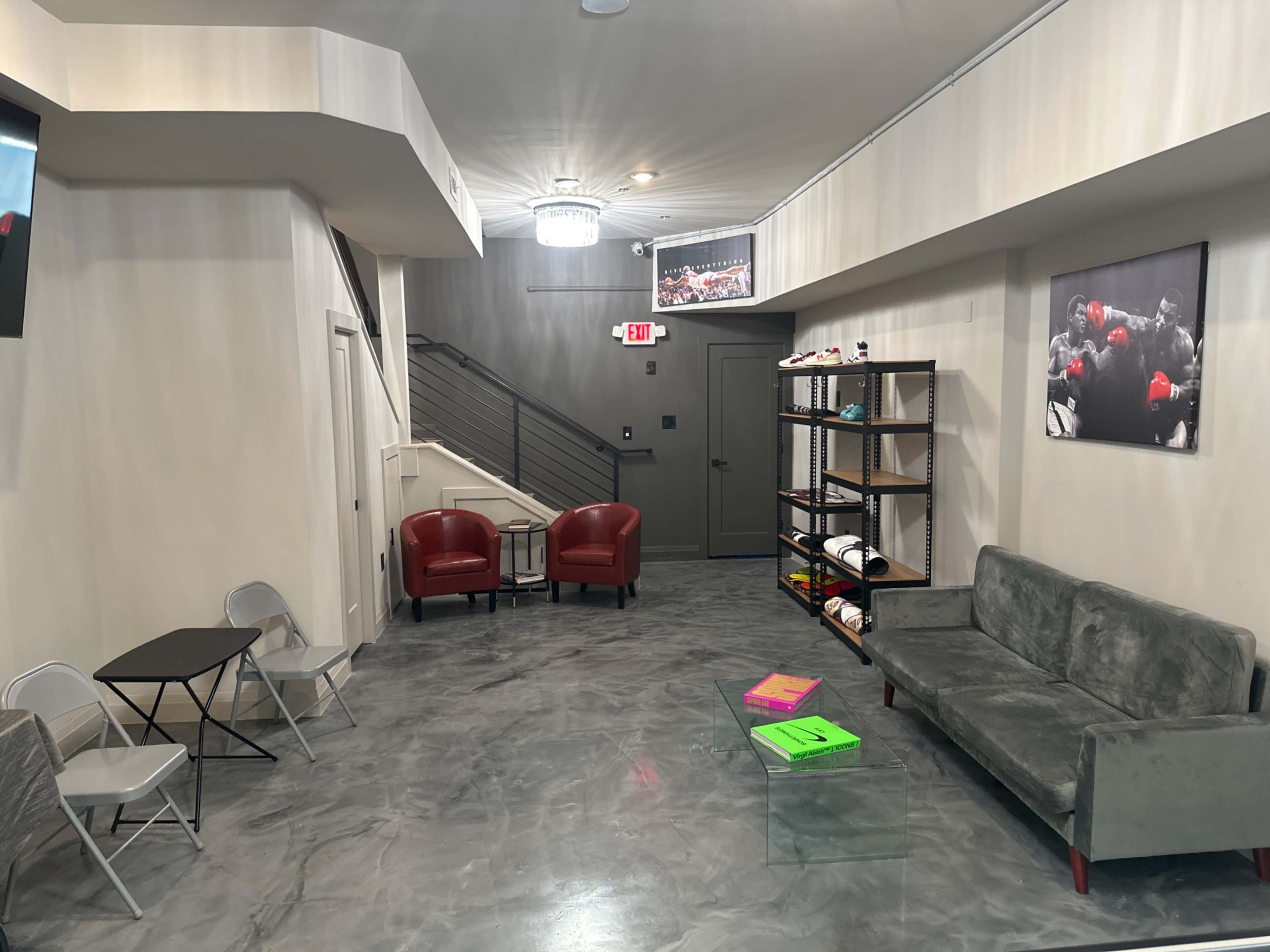 A modern interior space with gray walls, a seating area featuring a green sofa and red chairs, a small table, and a staircase in the background.