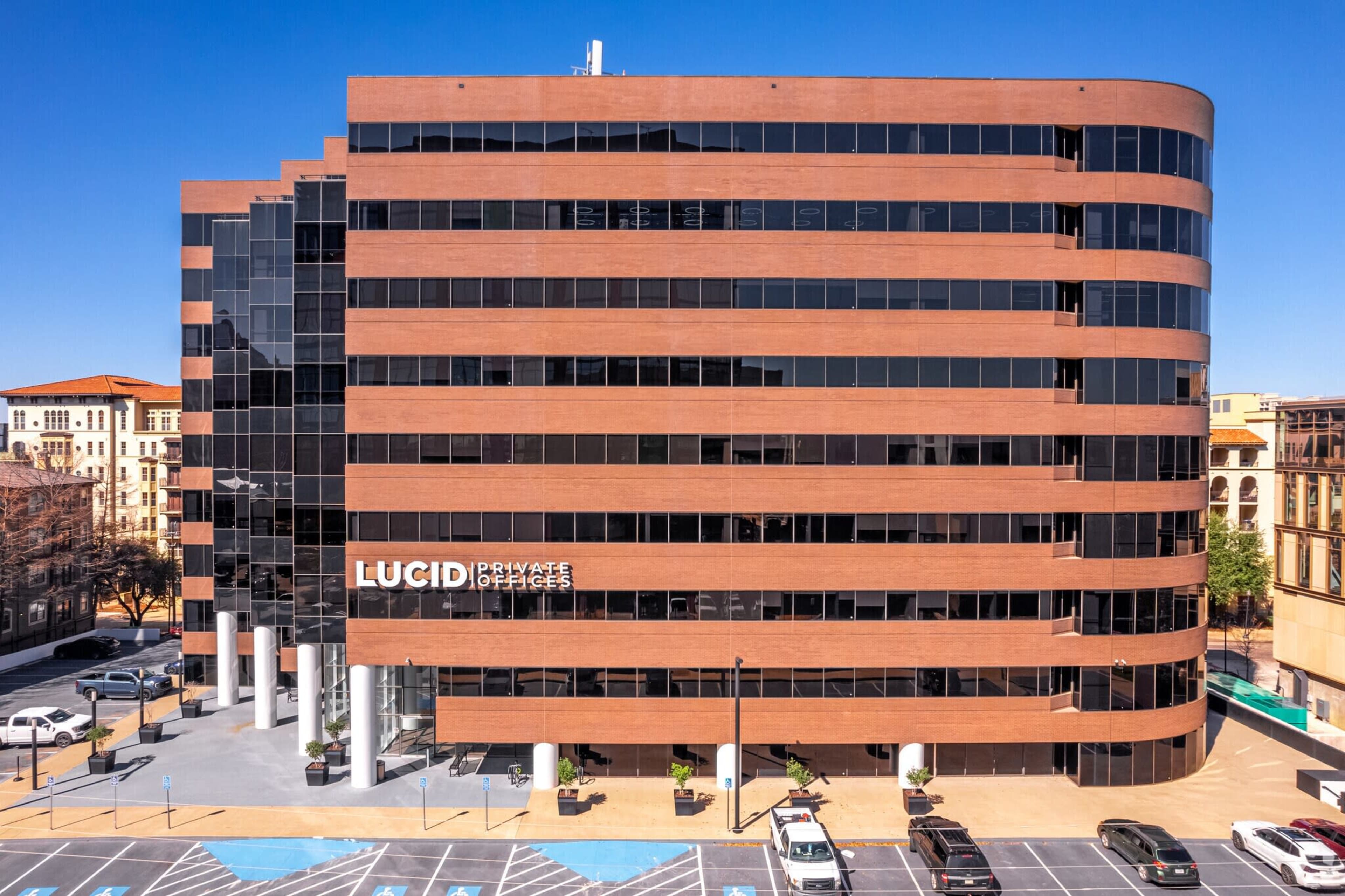 A modern office building with a brick exterior and large glass windows features the name "LUCID Private Offices" prominently displayed on its facade.