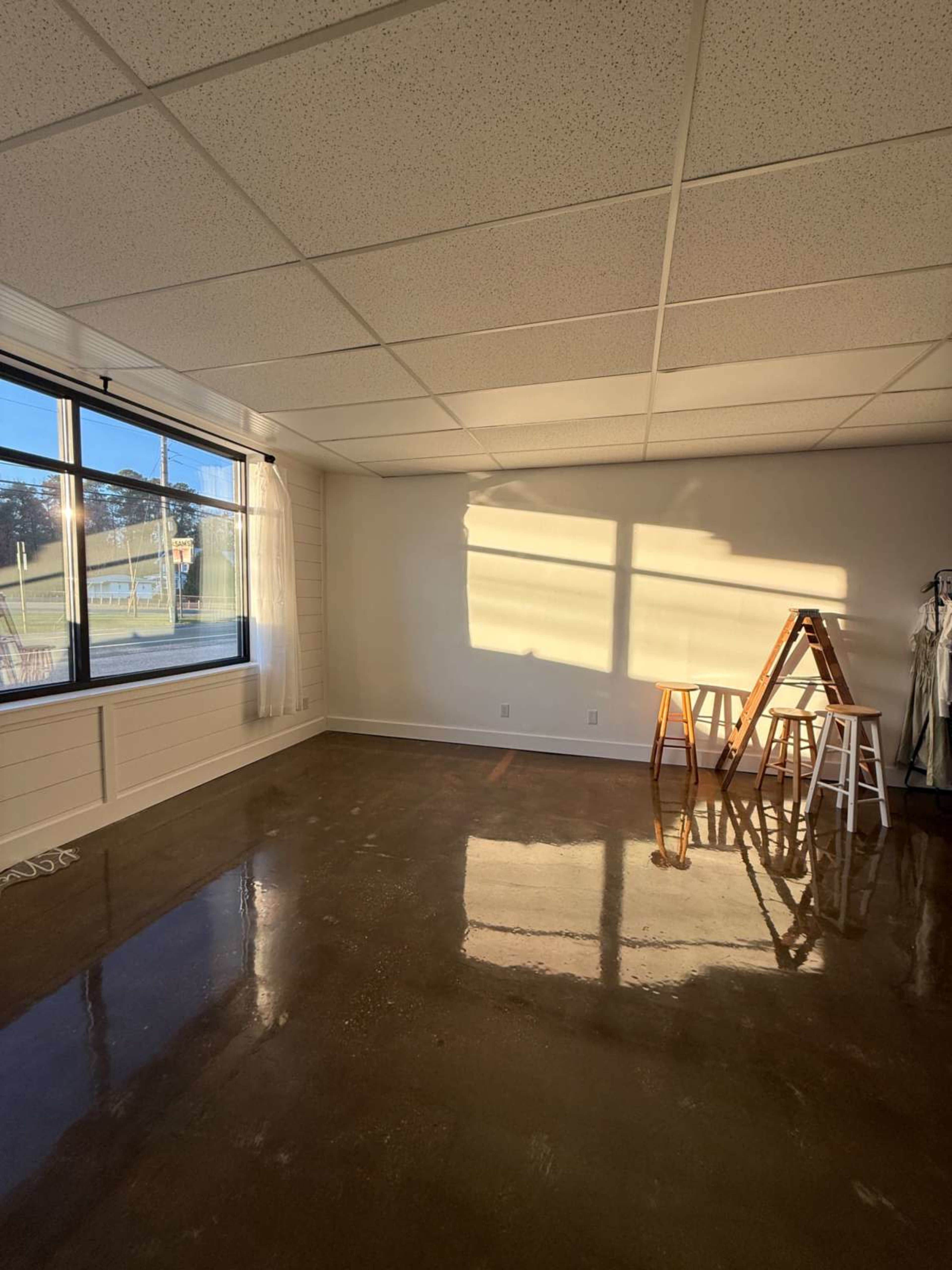 The image shows an empty room with a polished concrete floor, a window letting in natural light, and a ladder positioned against the wall.