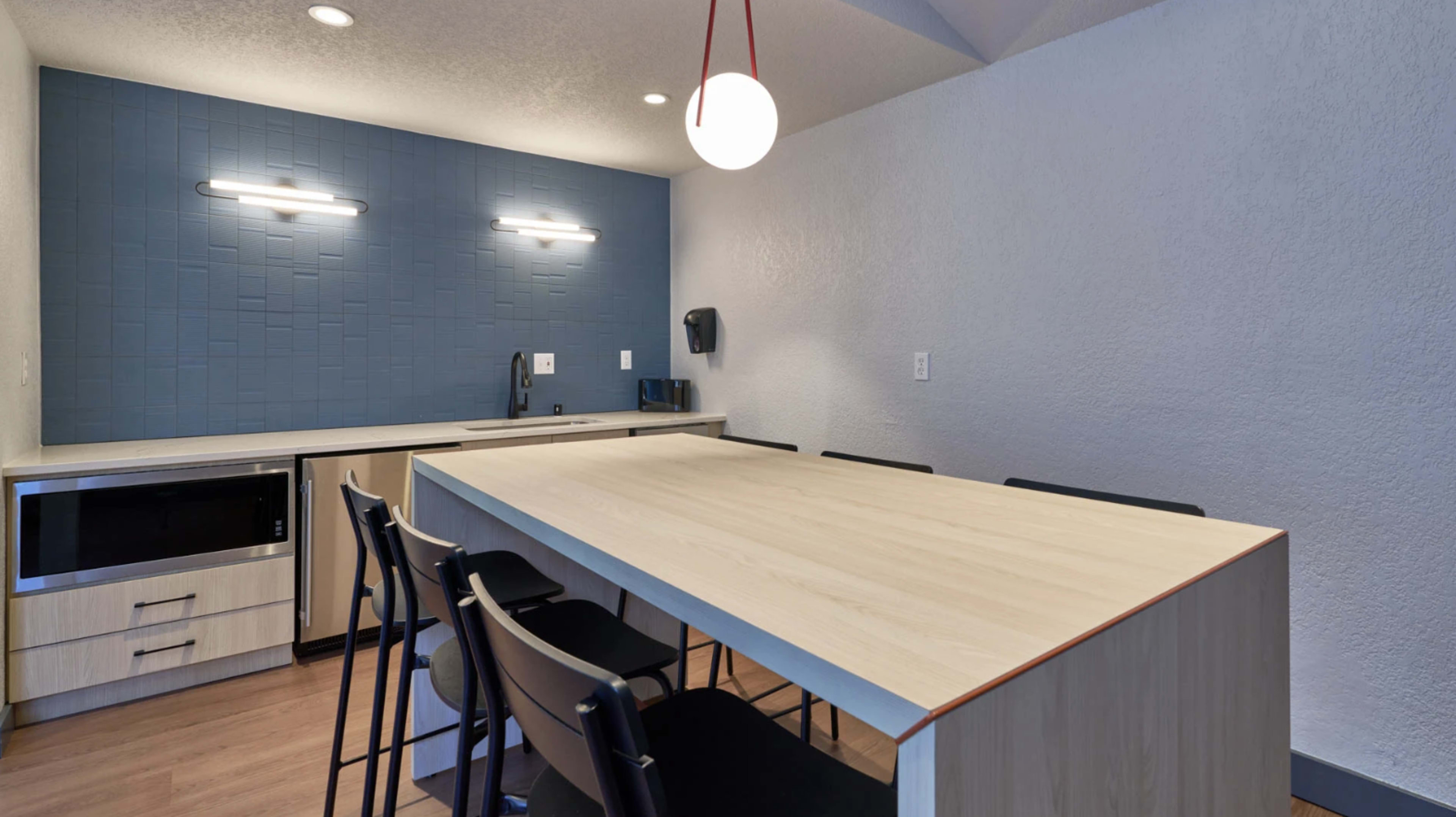 The image shows a modern kitchen with a large wooden table, black chairs, and a wall featuring a blue textured design.