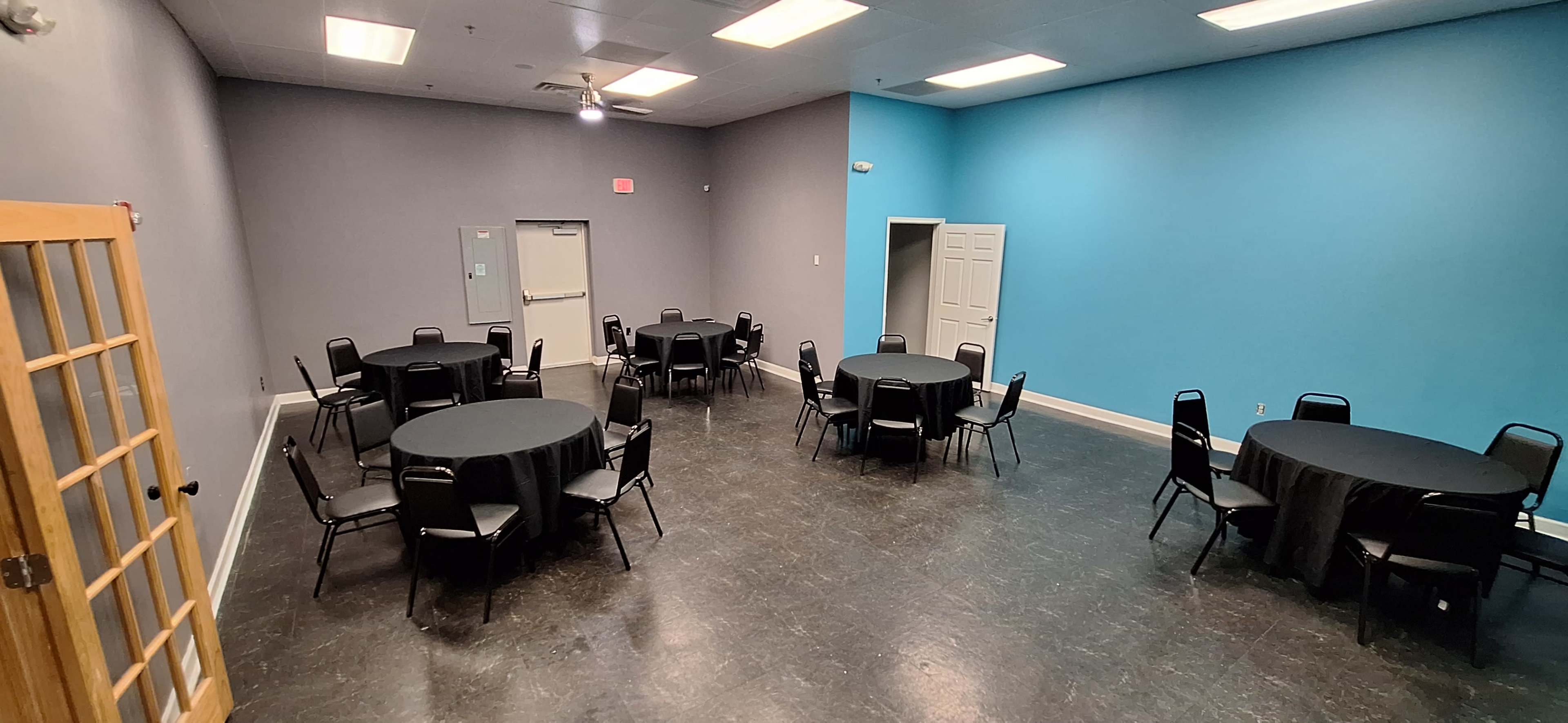 A large room with several round tables covered in black tablecloths, arranged around the space, and walls painted in gray and light blue.