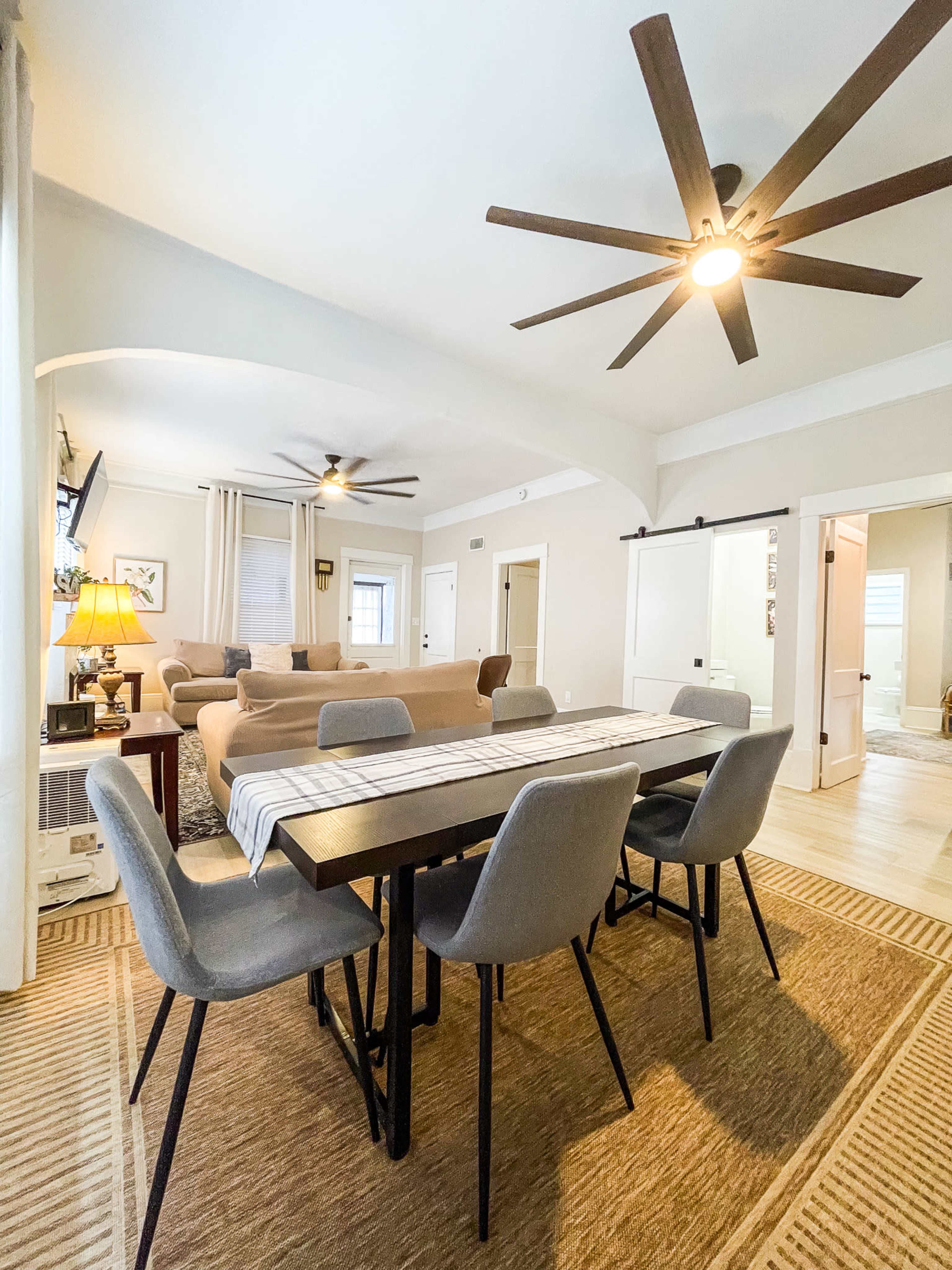 A dining area with a wooden table and gray chairs is positioned near a living space featuring a couch and overhead ceiling fans.