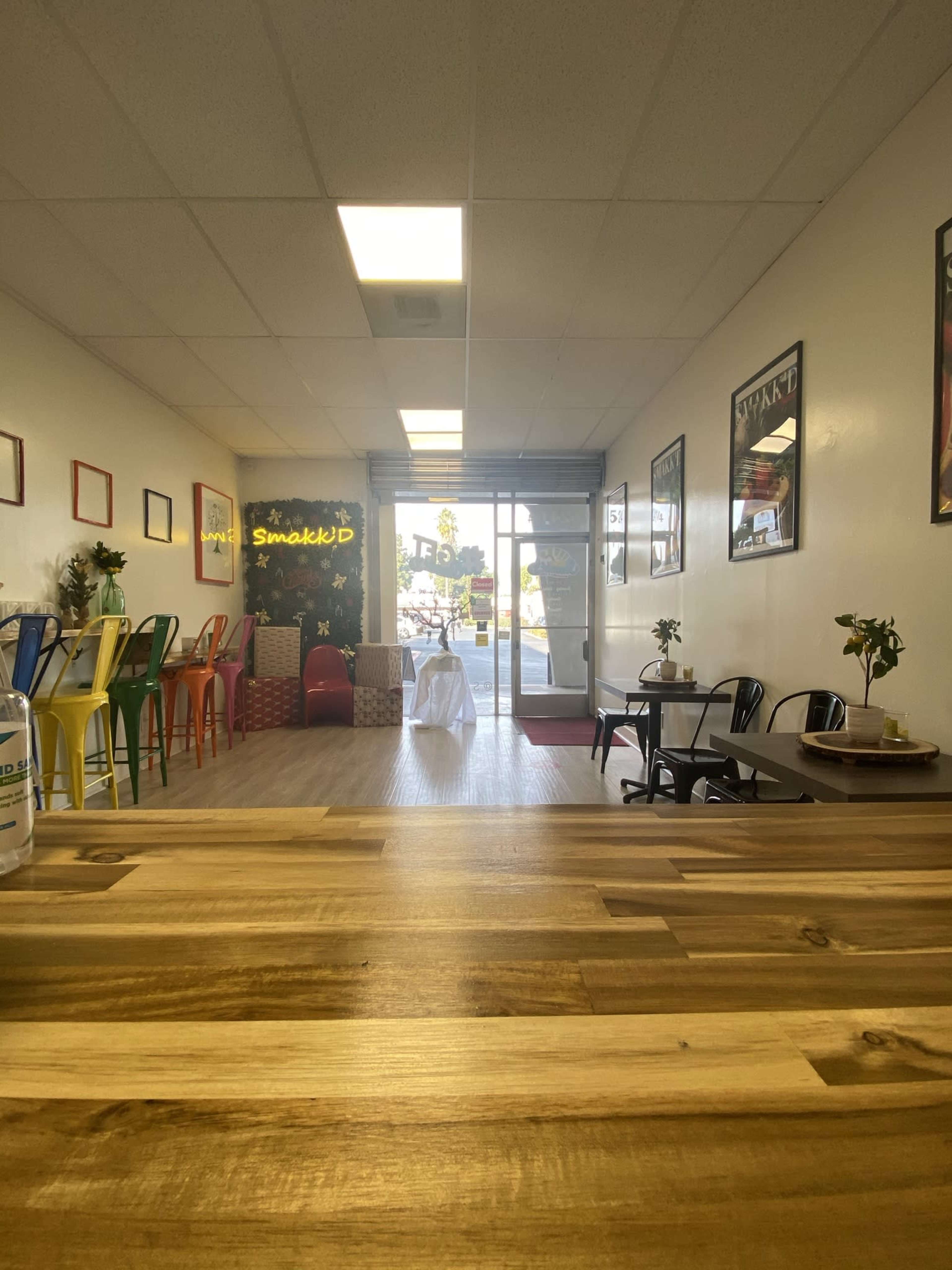 The interior of a café with colorful chairs, a counter made of wood, and a view of the street through the glass entrance.