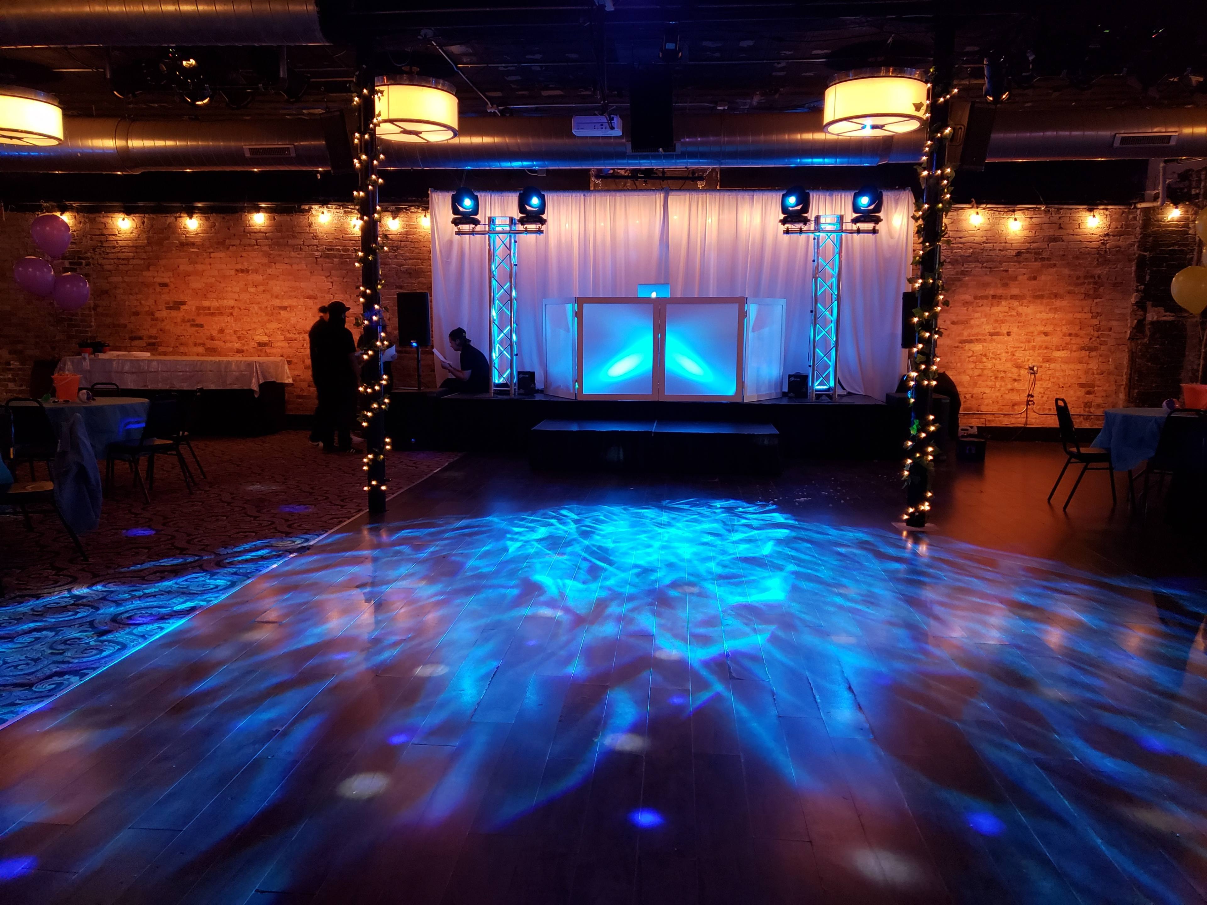 The image shows an empty event space with a dance floor illuminated by blue lights and decorated with string lights along the walls.