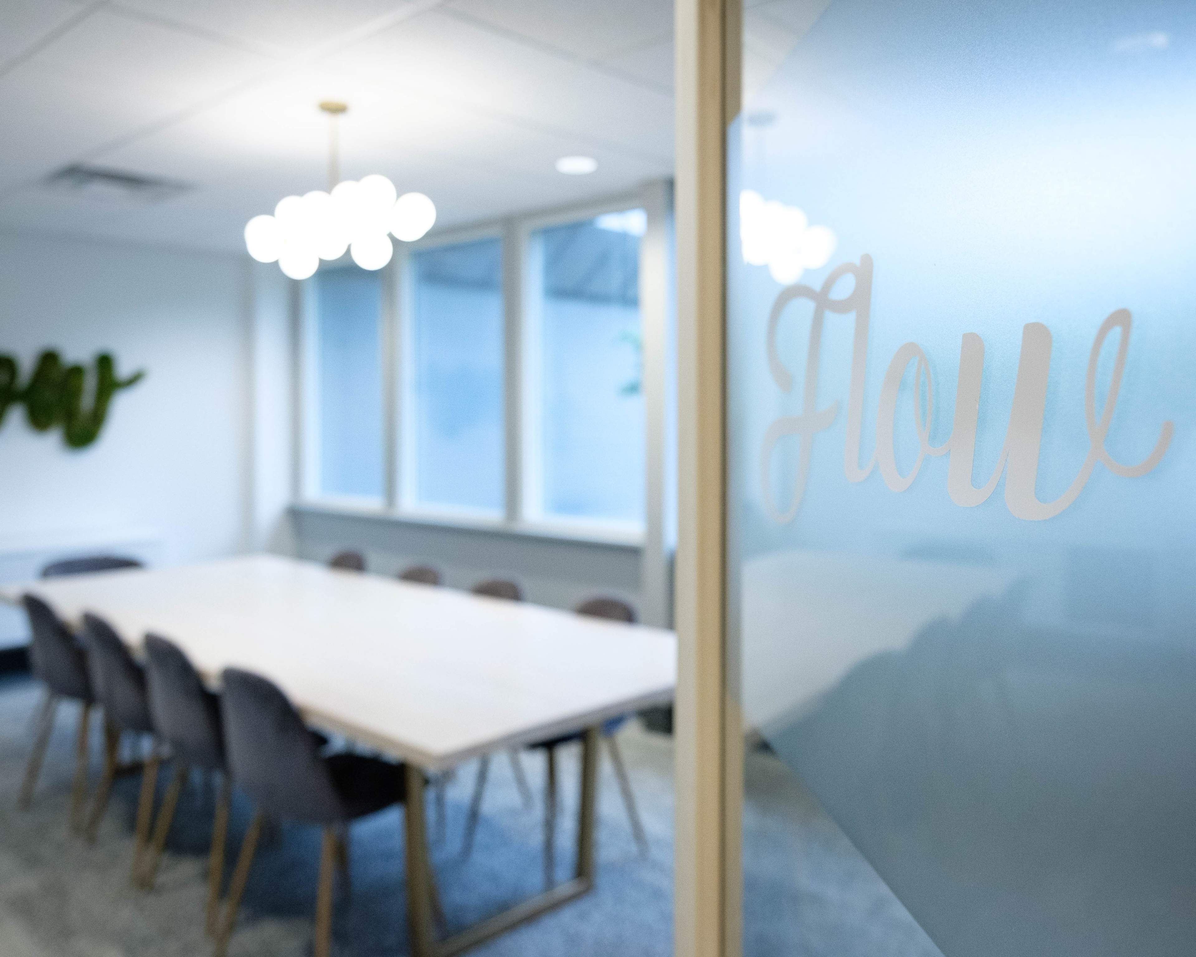 A conference room with a long table surrounded by chairs, illuminated by pendant lights and featuring large windows.