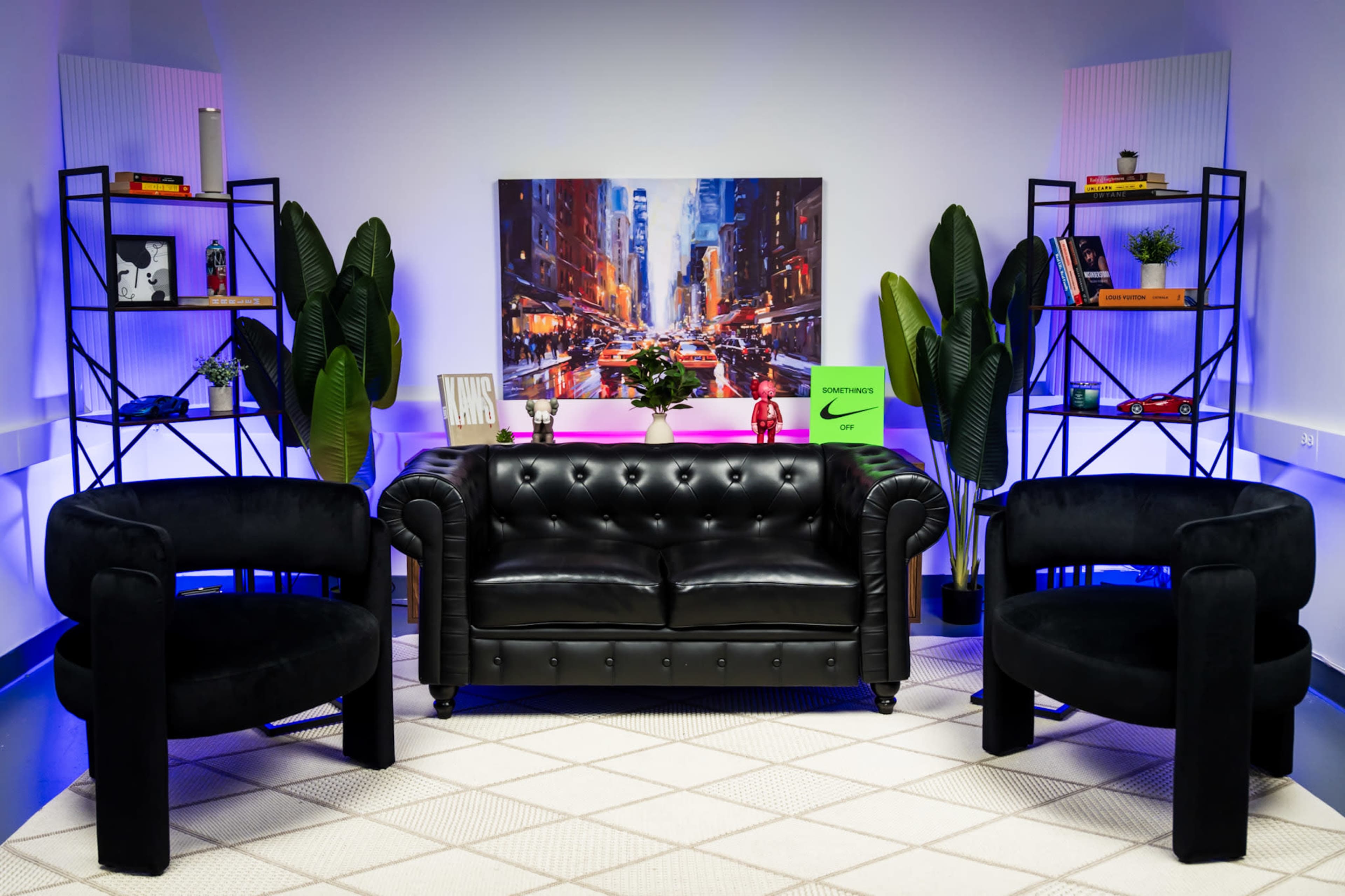 The image shows a modern living room setup with a black leather sofa and two matching circular chairs, surrounded by potted plants and shelves displaying various decorative items.