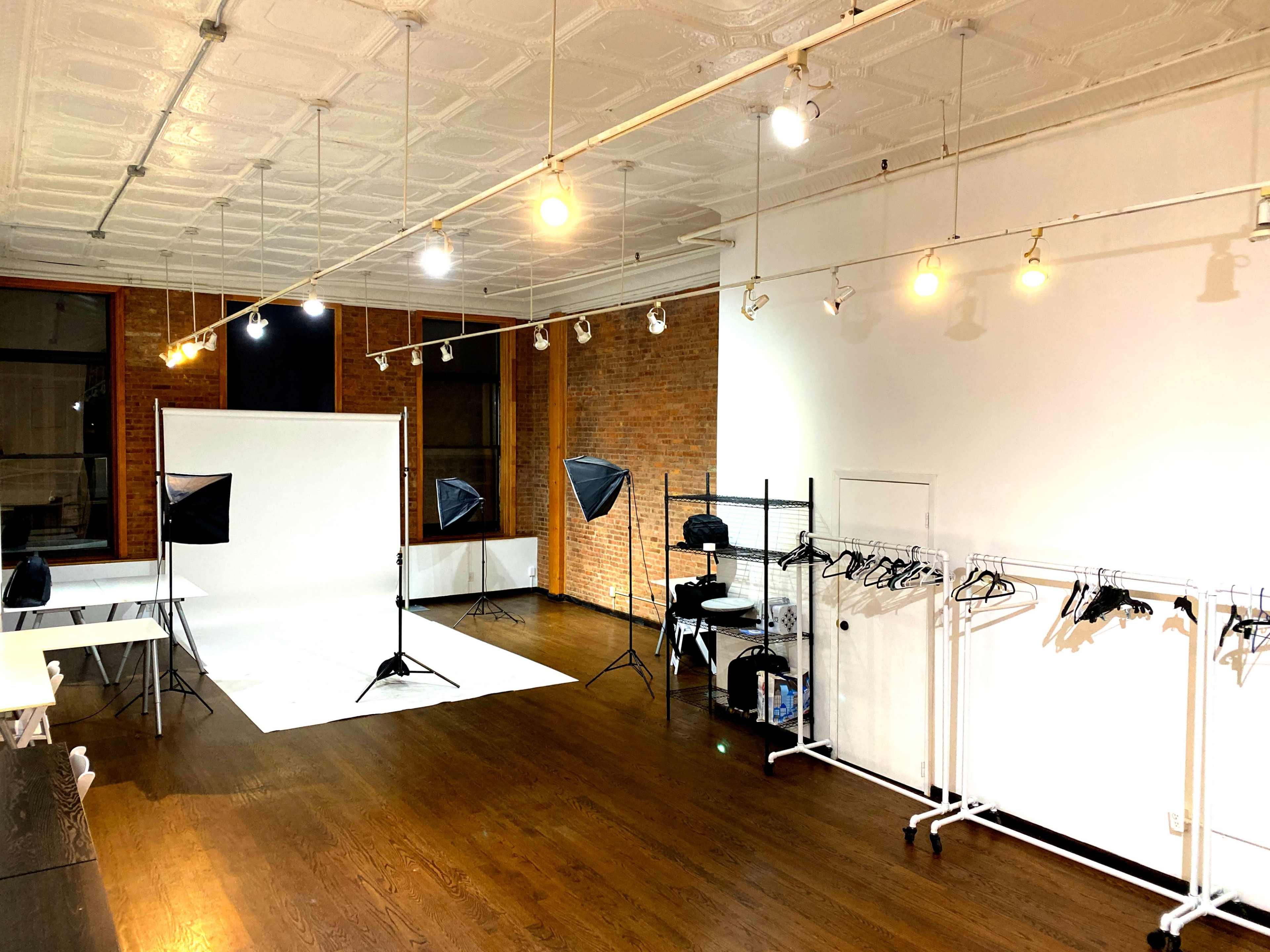A photography studio with a white backdrop and multiple lighting setups, along with clothing racks along the wall.
