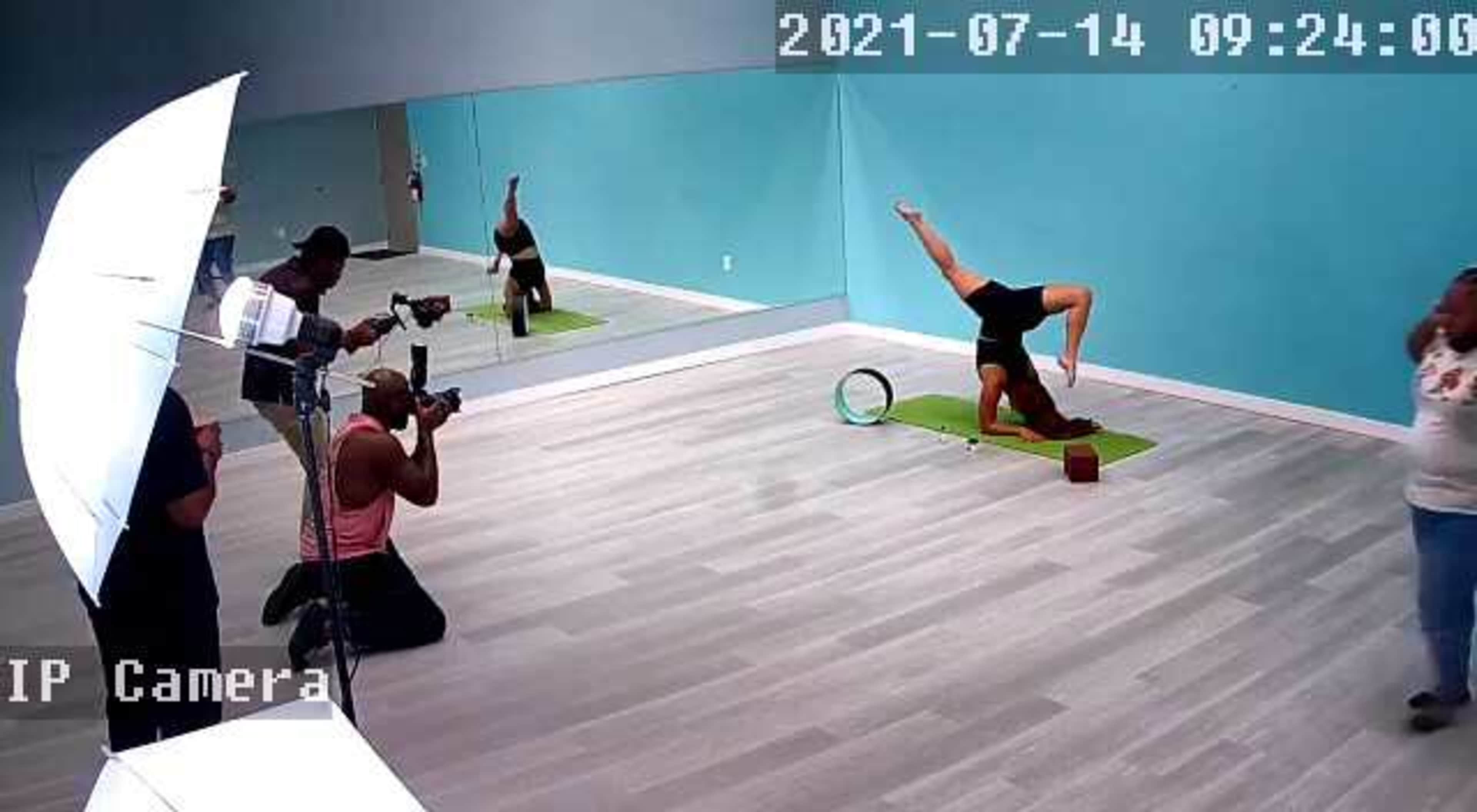 A person performs a yoga pose on a mat while two photographers capture images in a brightly lit studio.