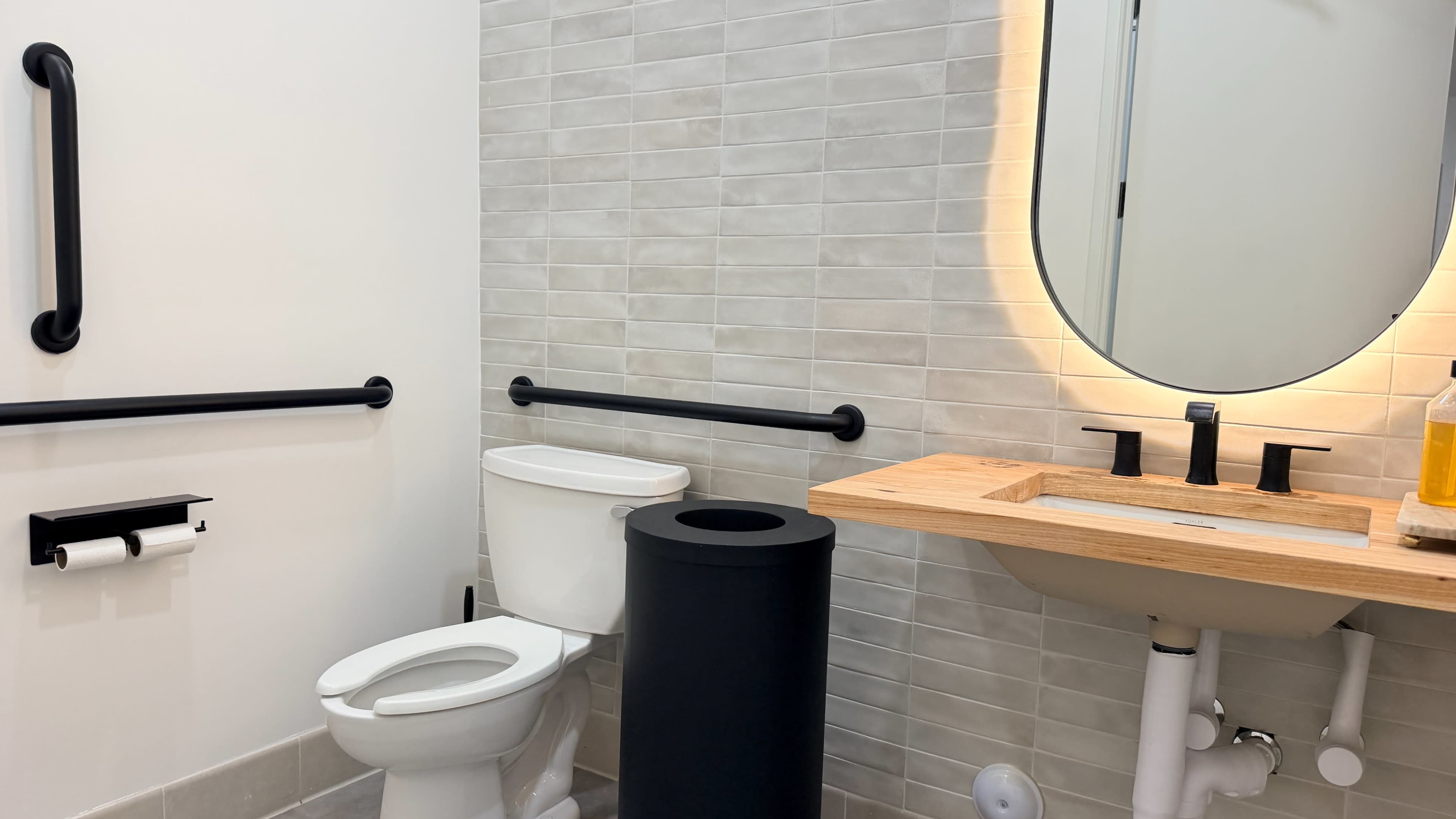 The image shows a modern bathroom featuring a toilet, a sleek sink with a wooden countertop, and a circular mirror above it.