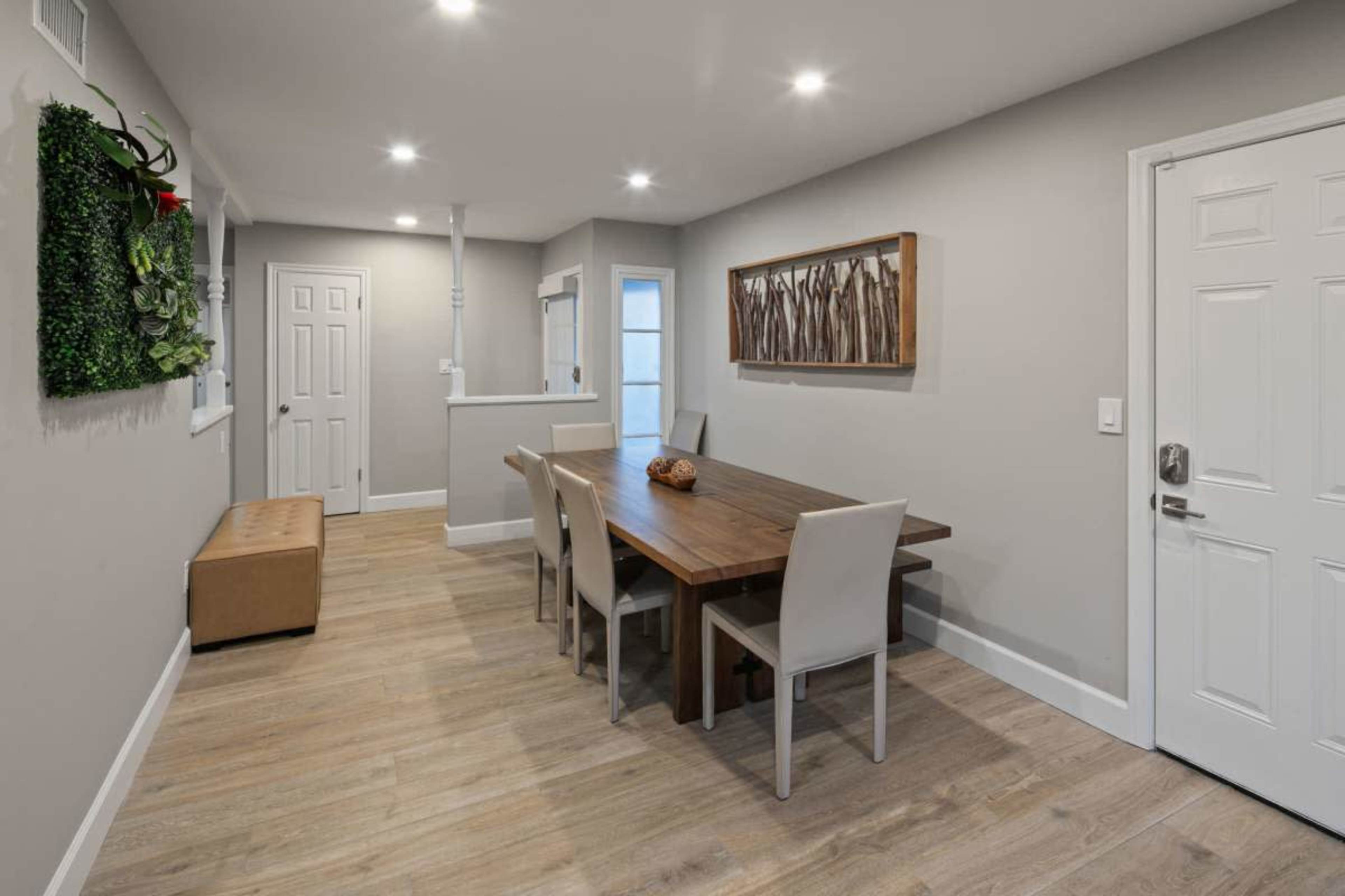 A dining area features a wooden table surrounded by four chairs, with a bench and decorative wall art in a neutral-toned room.