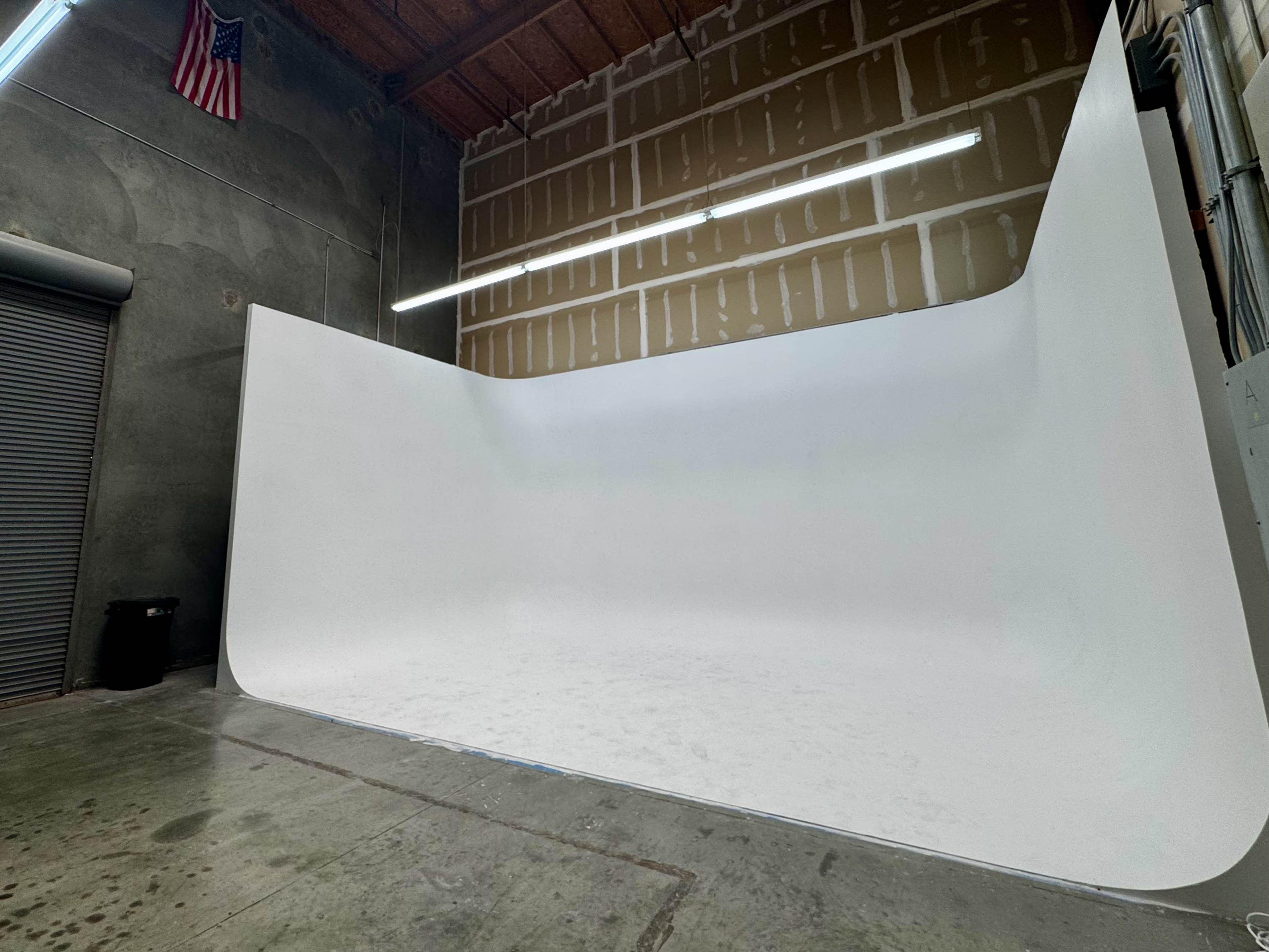 The image shows a spacious studio with a curved white backdrop and bare concrete flooring, illuminated by overhead lights.