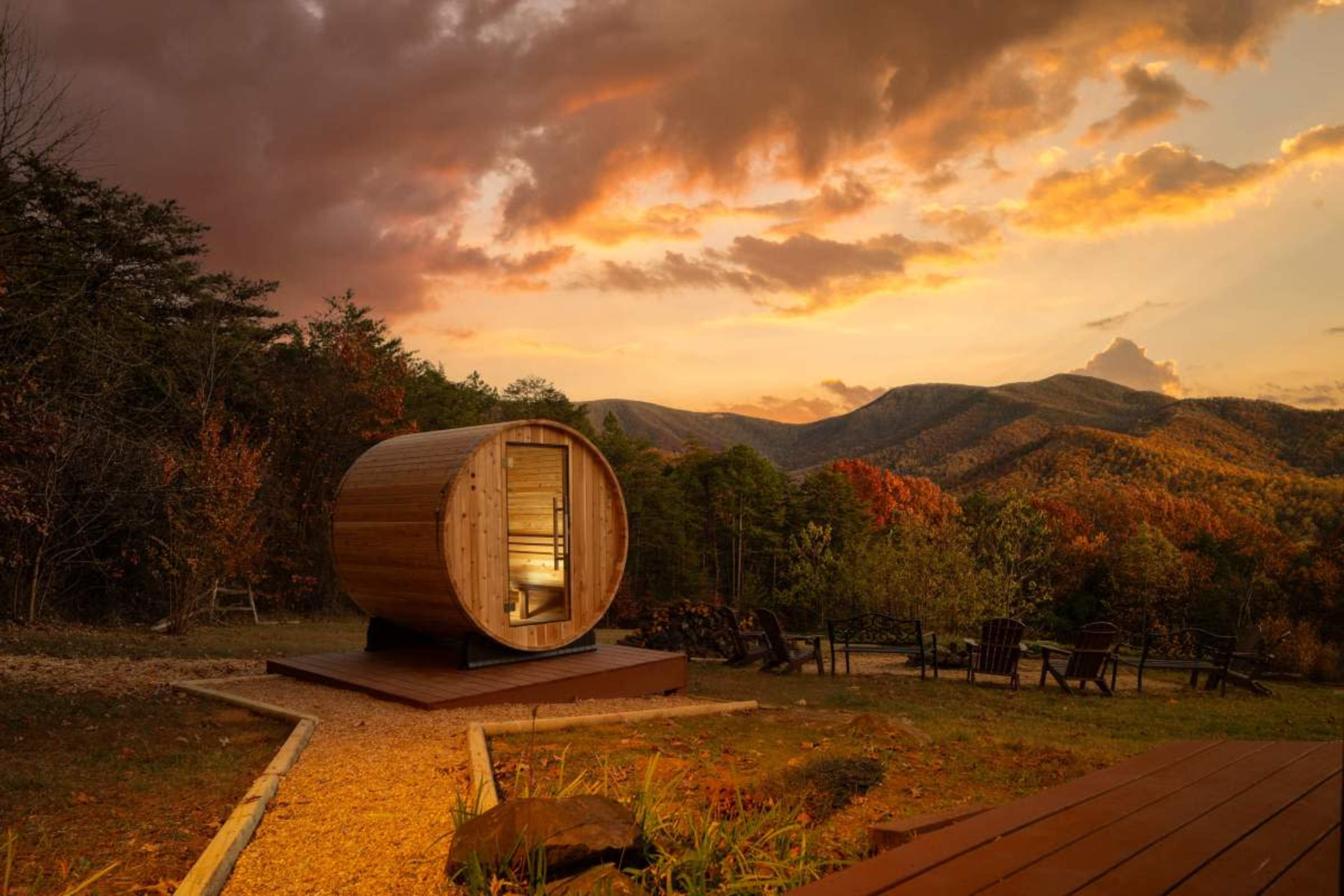 A cylindrical wooden cabin sits on a platform overlooking mountains under a colorful sunset sky.