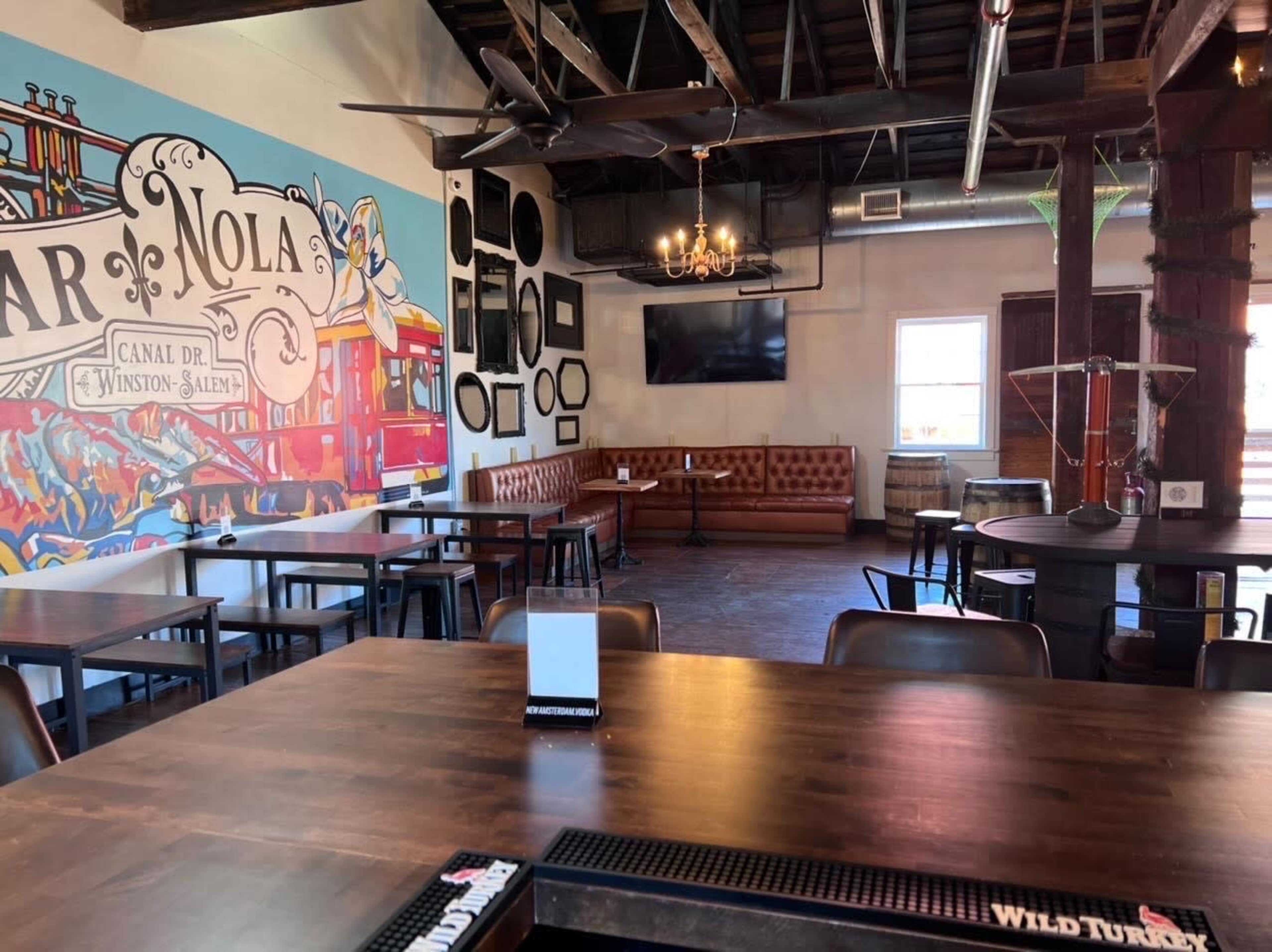 A spacious, rustic interior of a restaurant or bar with a mural on one wall, wooden tables, and a leather sofa area.