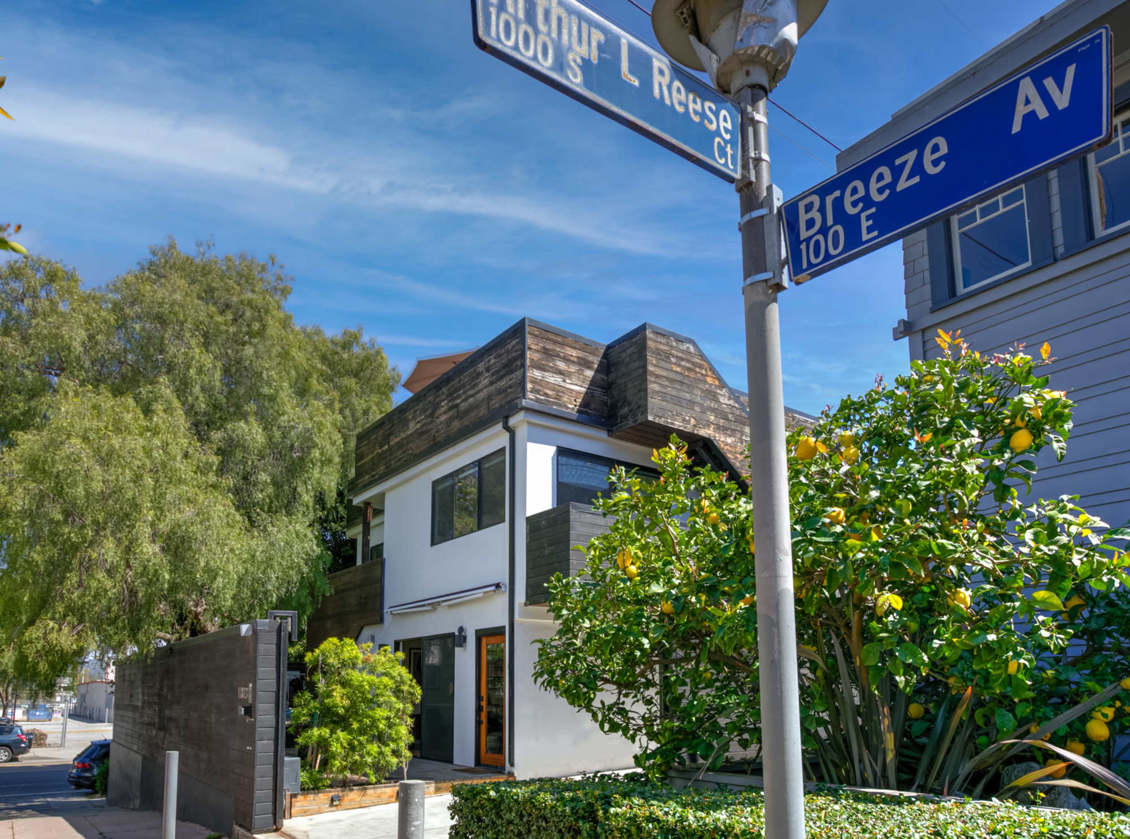 The image shows a modern house at the intersection of Arthur L. Reese Court and Breeze Avenue, surrounded by greenery and a clear blue sky.