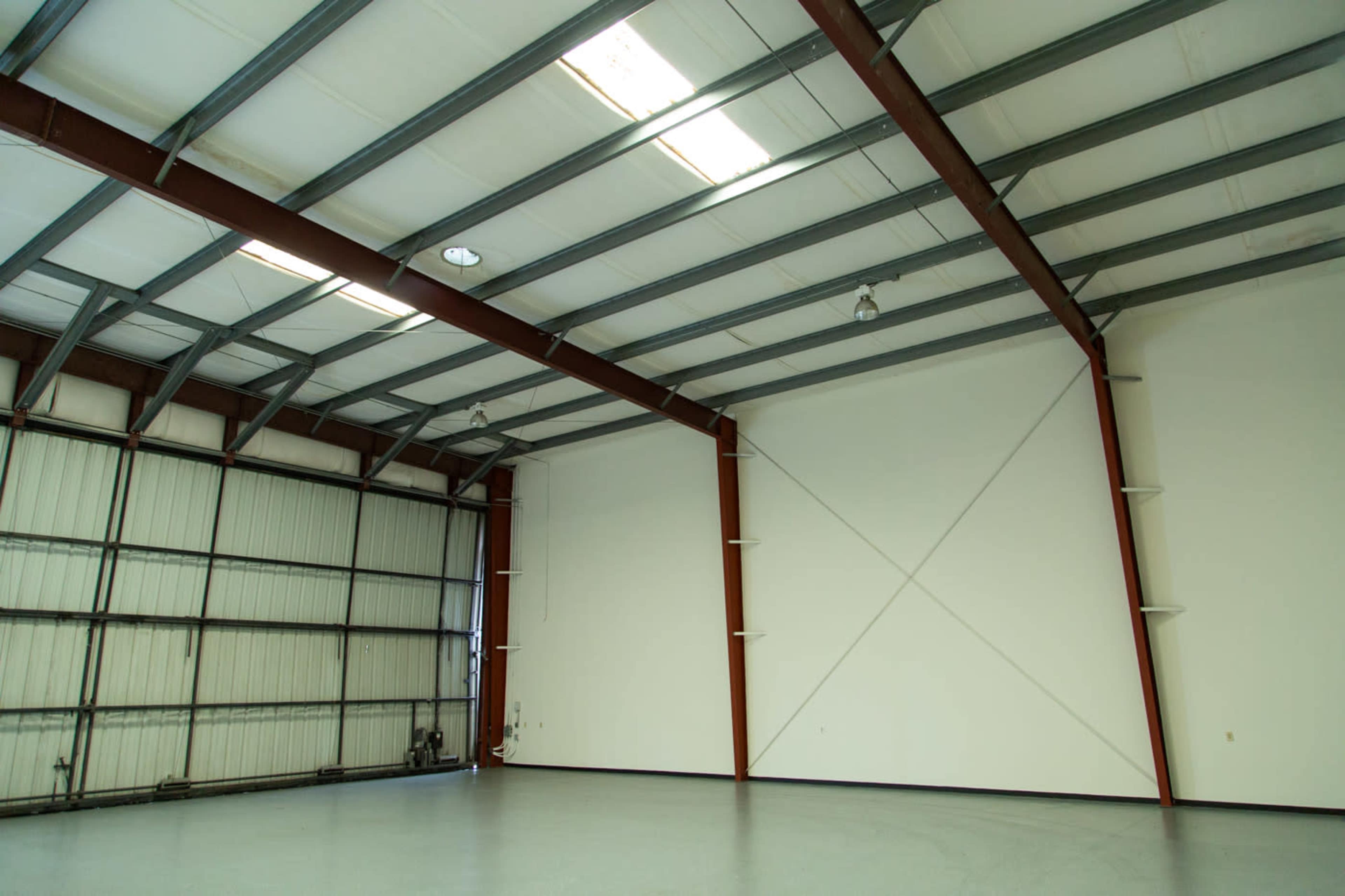 A spacious industrial interior with metal beams, a high ceiling, and a large unobstructed wall.