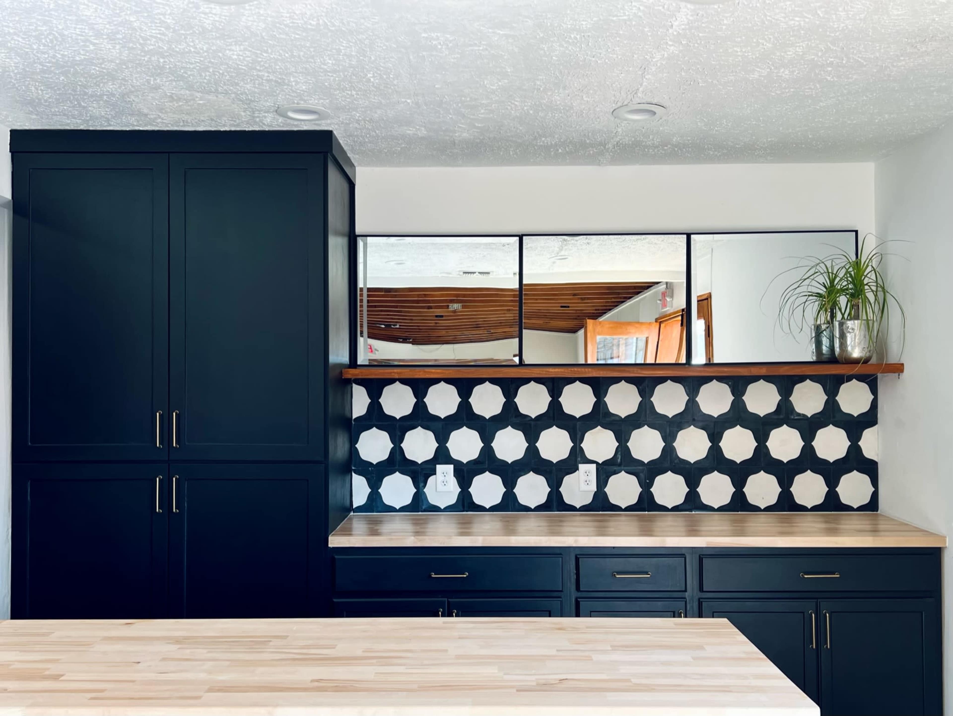 A modern kitchen featuring dark cabinetry, a light wooden countertop, and a backsplash with a geometric, black-and-white tile pattern.
