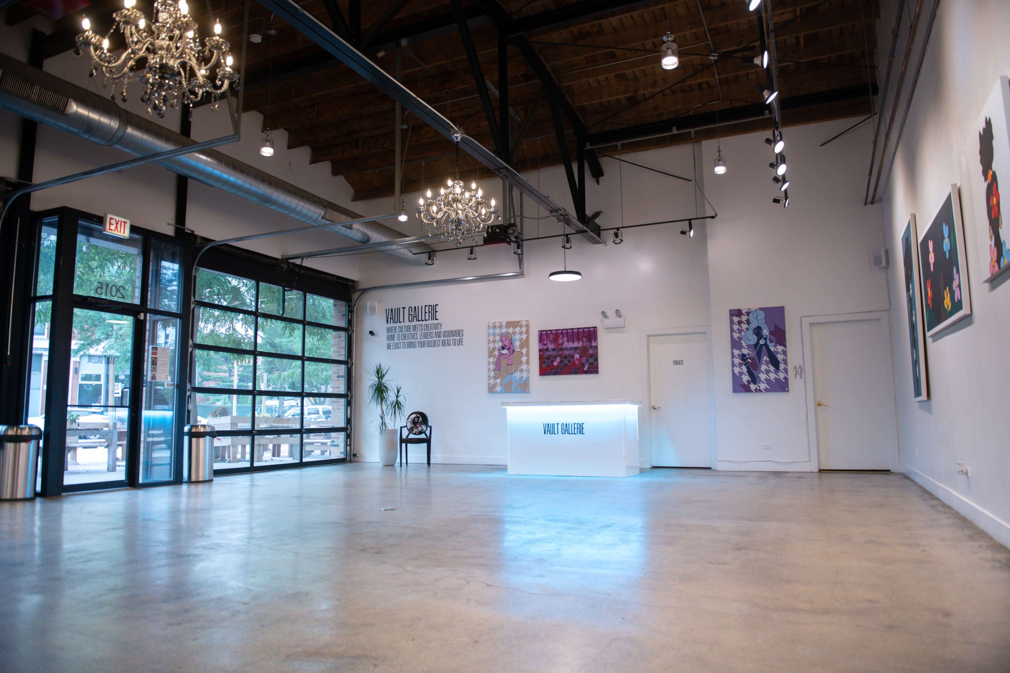 The image shows a modern, spacious art gallery with a wooden ceiling, minimalist decor, and illuminated artwork on the white walls.