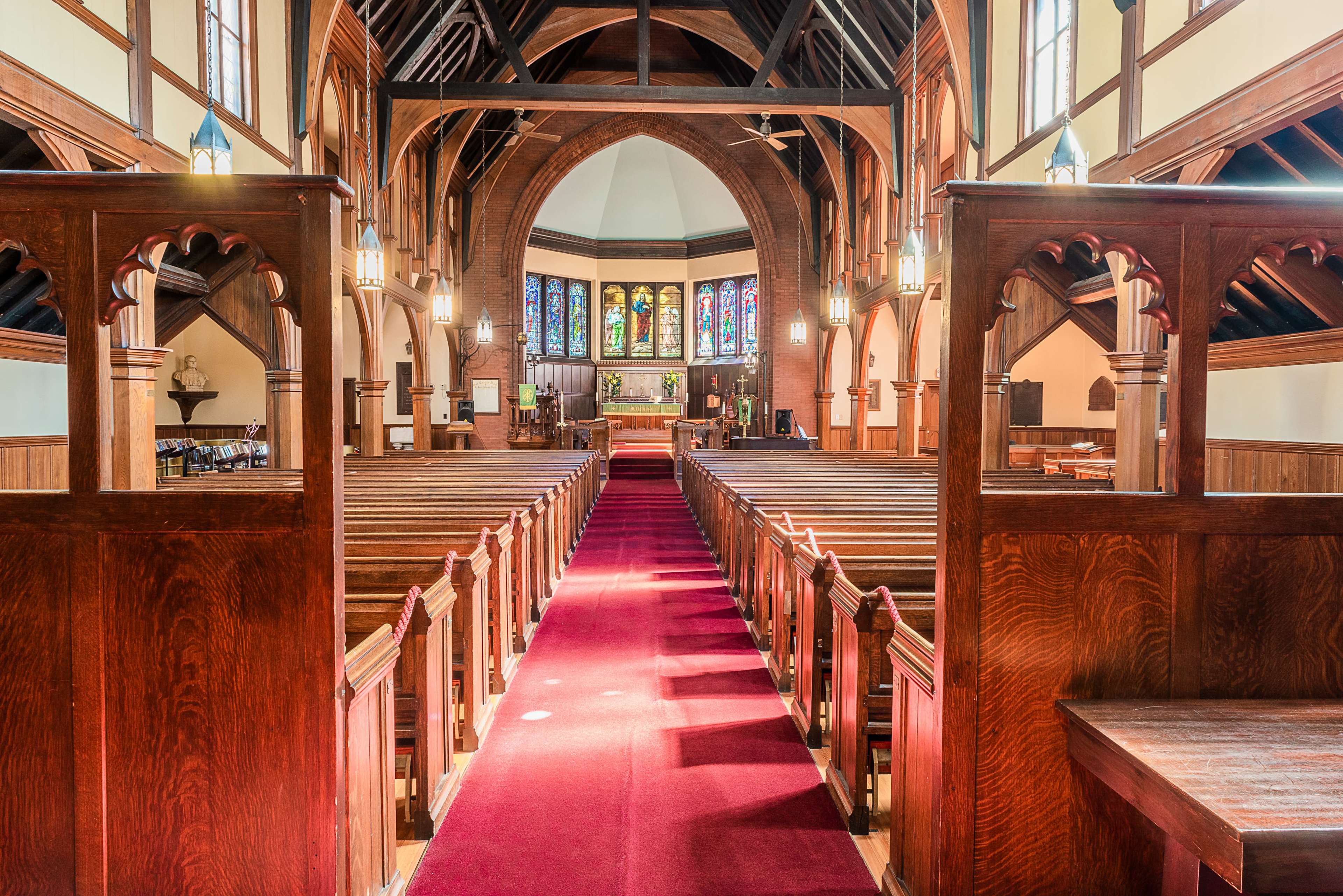 The interior of a church featuring wooden pews arranged along a central aisle, with stained glass windows and a raised altar at the front.