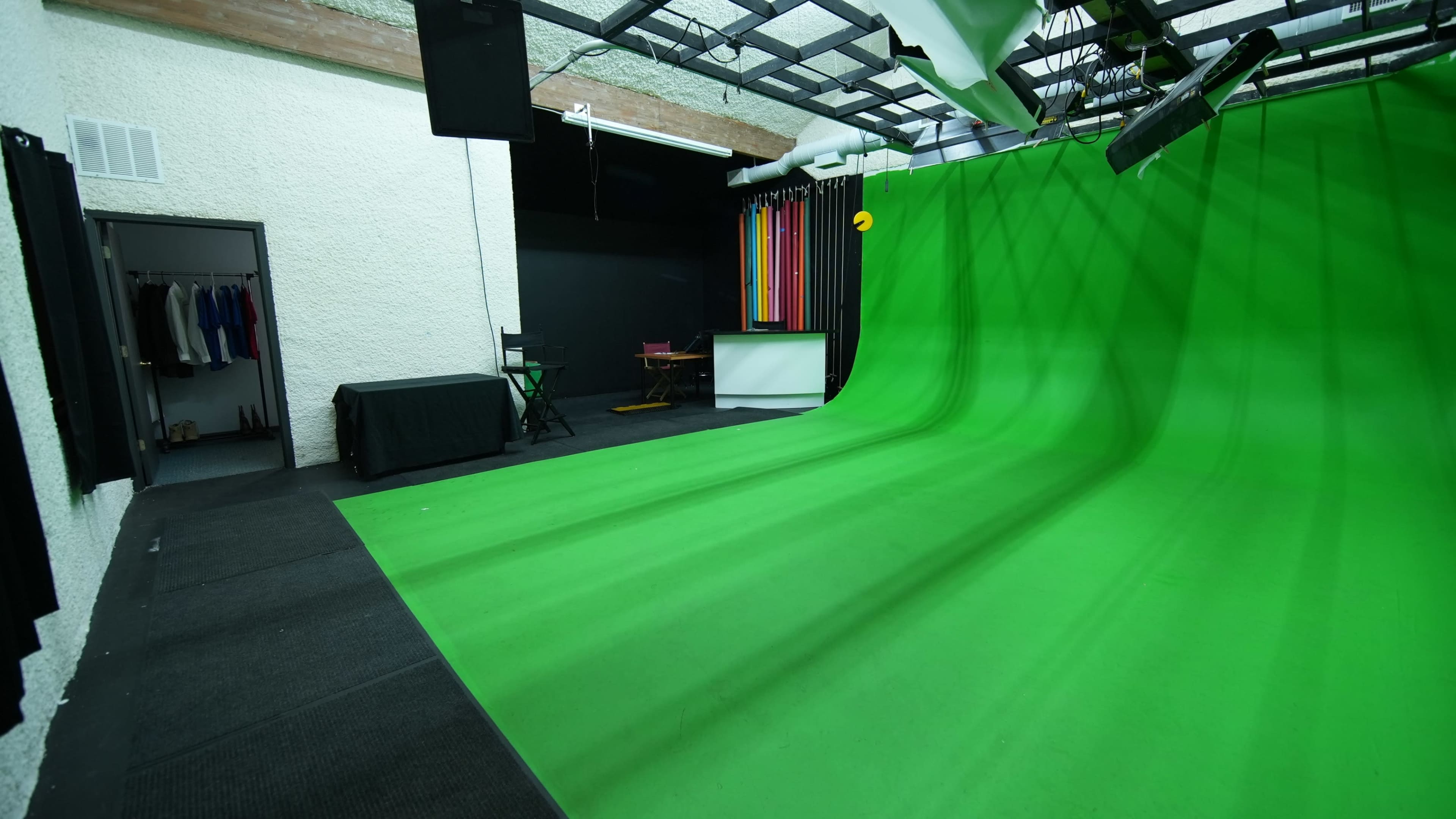 The image shows a green screen studio with a large green backdrop, black curtains, and various equipment arranged throughout the space.