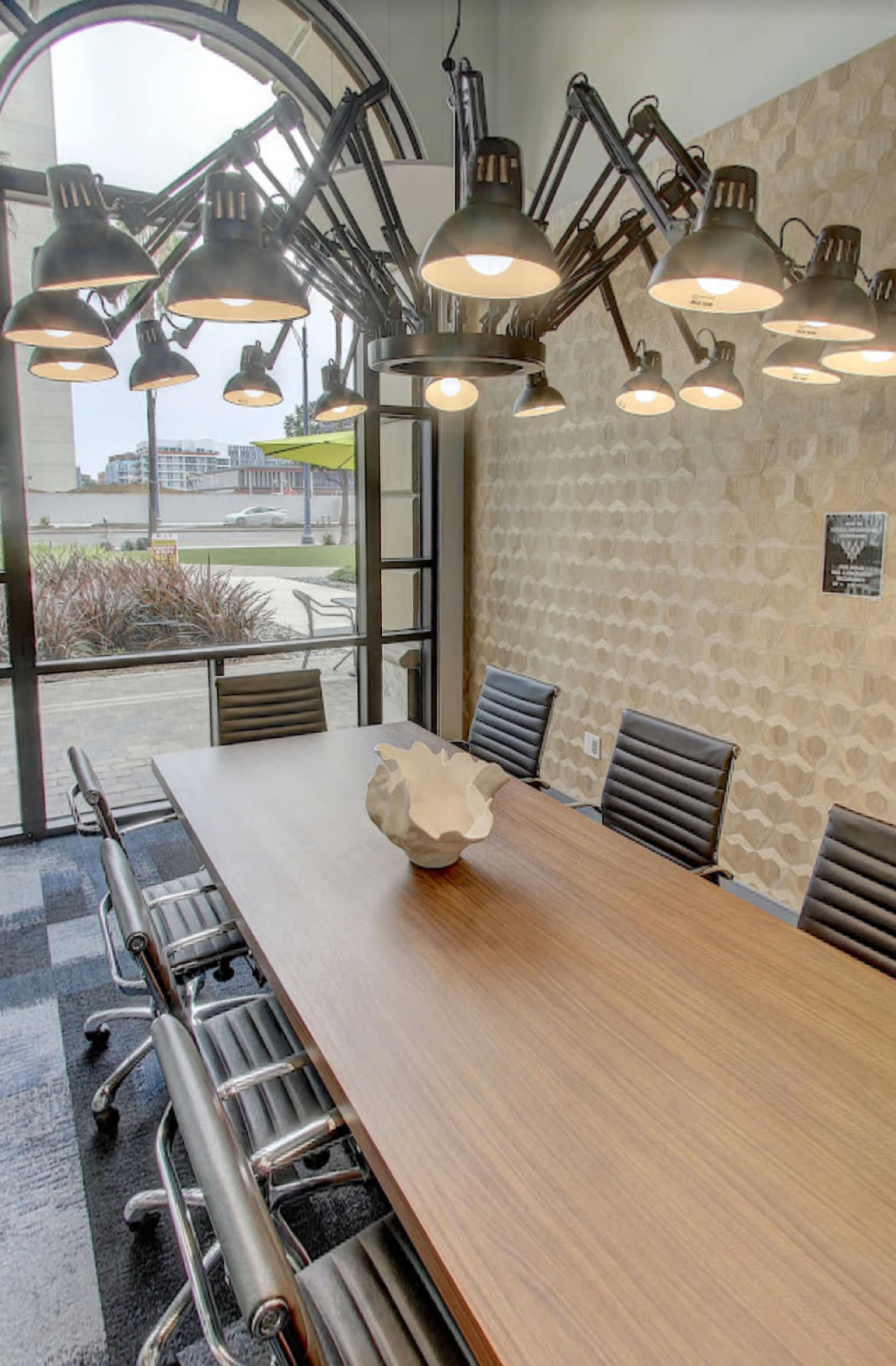 A large conference room features a wooden table surrounded by metal chairs, illuminated by an elaborate hanging light fixture.