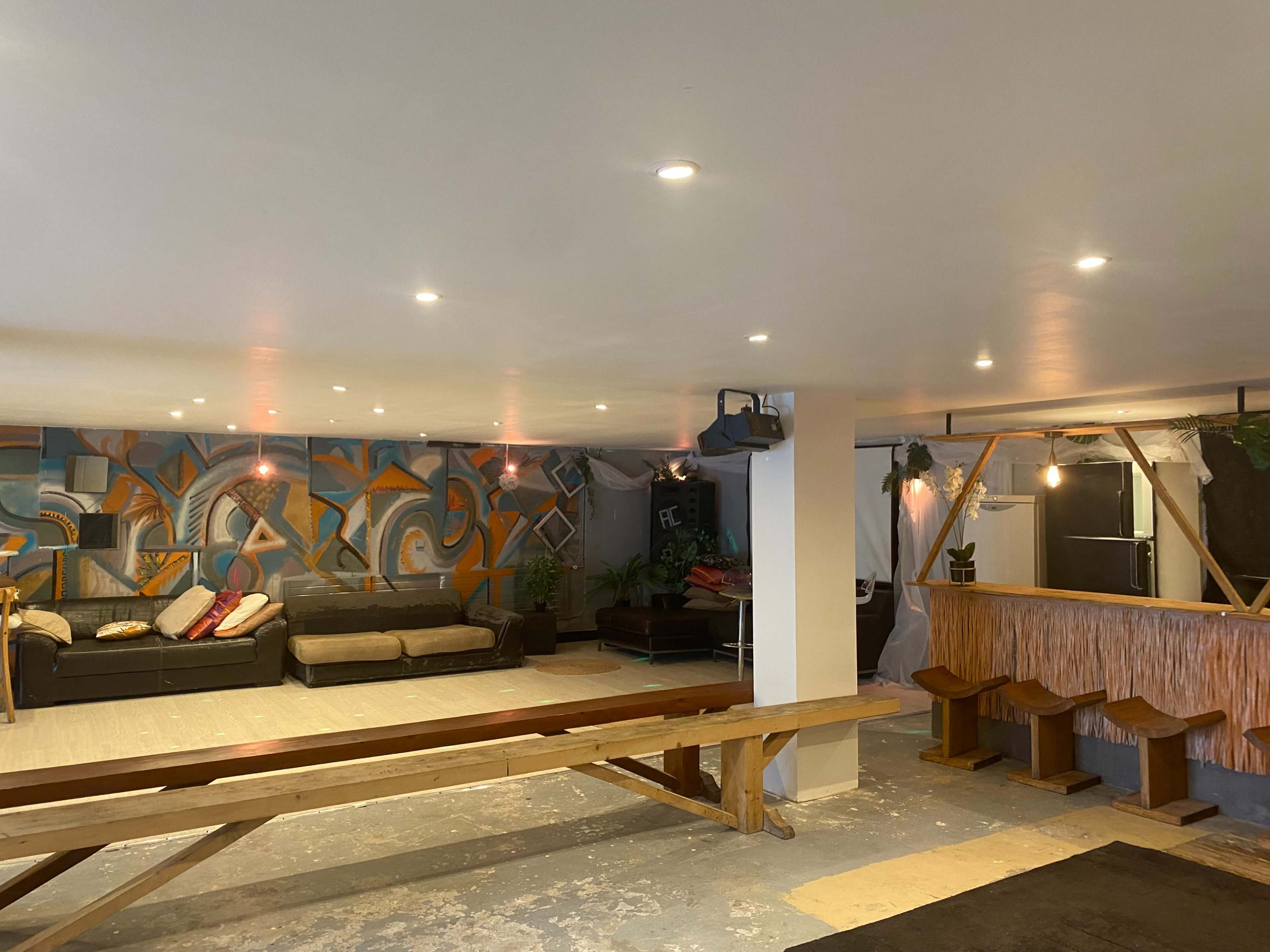 The image shows a spacious lounge area with a bar, featuring colorful wall murals and seating arrangements.
