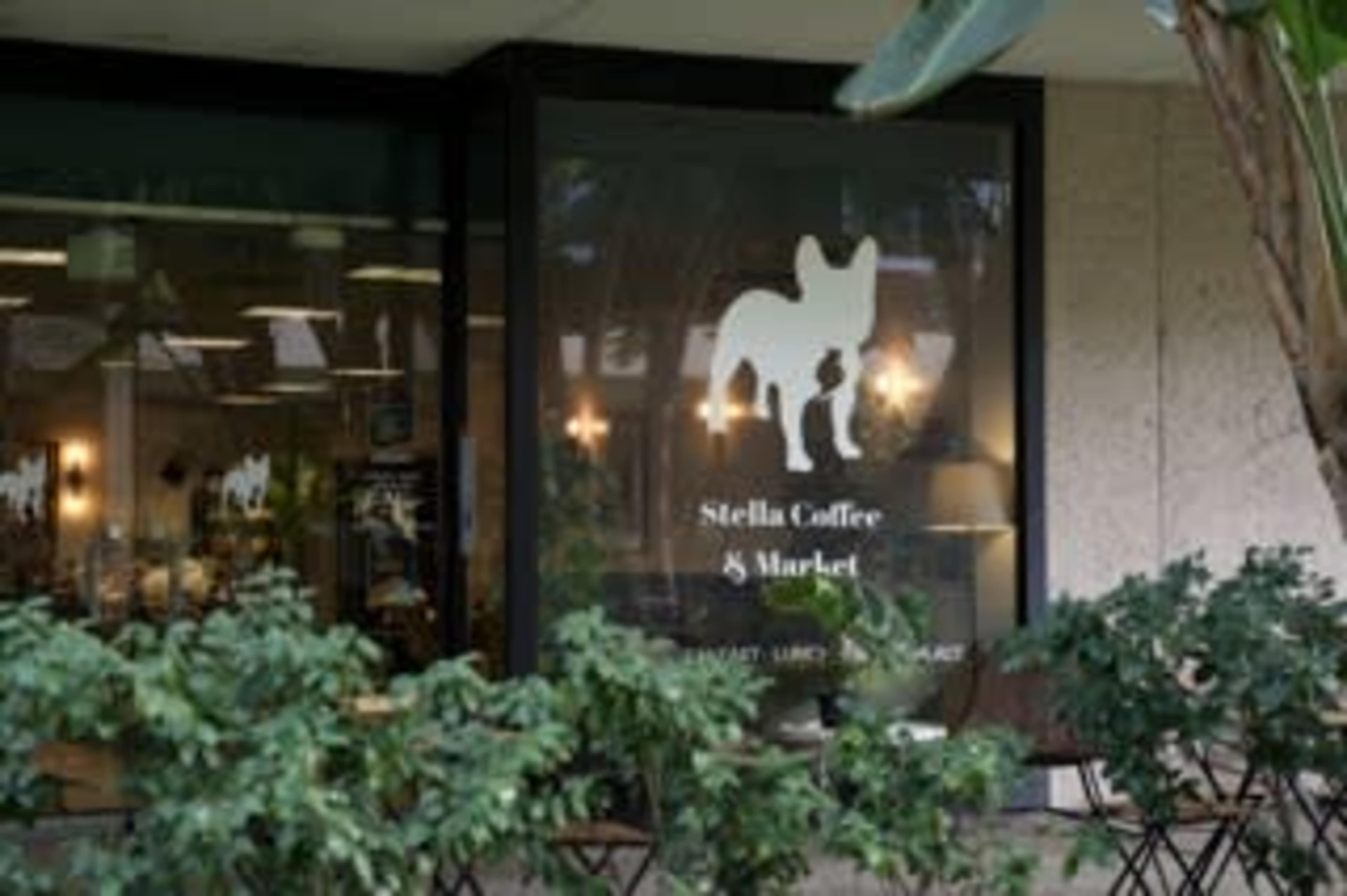 The image shows a storefront featuring "Stella Coffee & Market," with a silhouette of a dog in the window and outdoor seating in front.