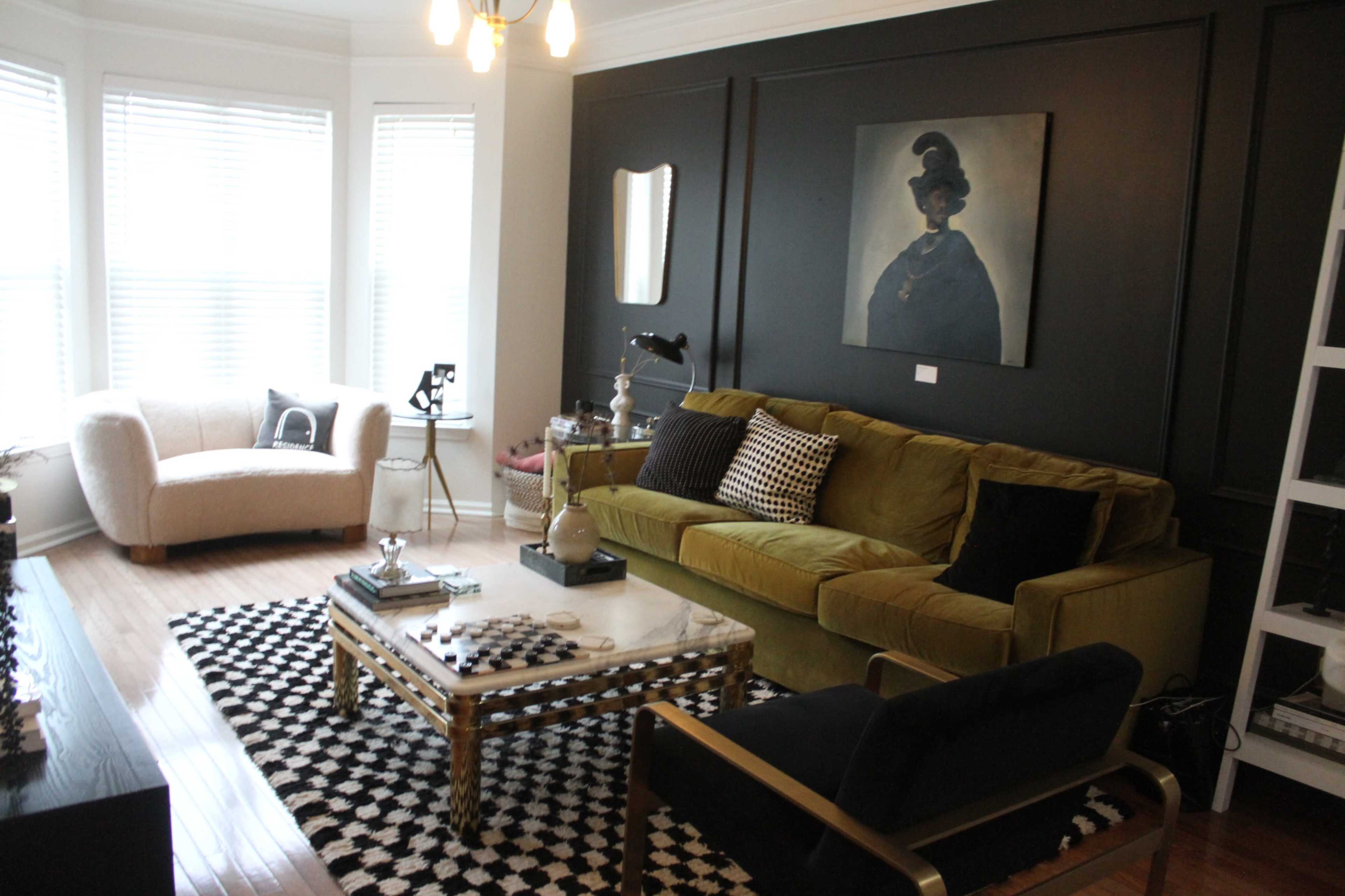 The living room features a green velvet sofa, a black and white patterned rug, and a large framed portrait hanging above a coffee table.