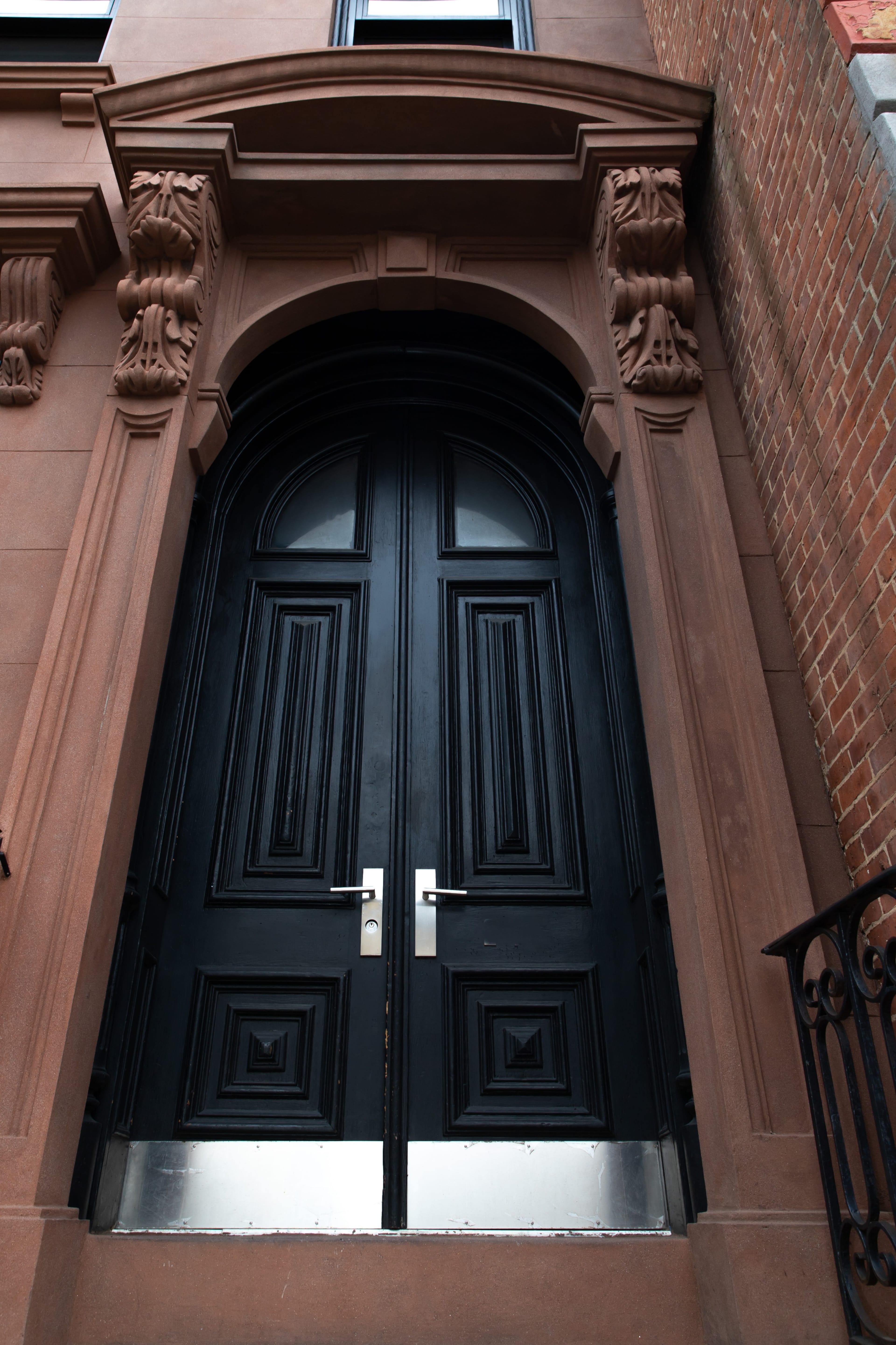 A large black double door with intricate carvings, set within a stone archway on a brick building.