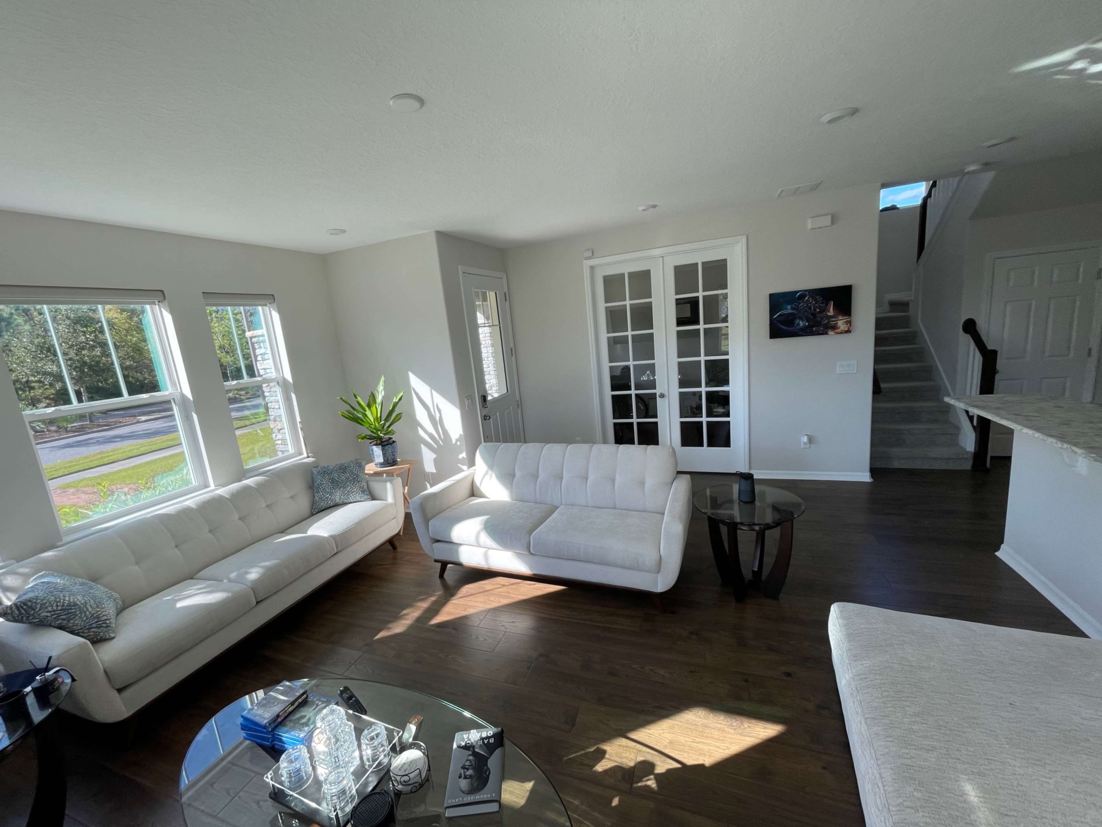 A modern living room with two white sofas, a glass coffee table, and large windows allowing natural light to fill the space.