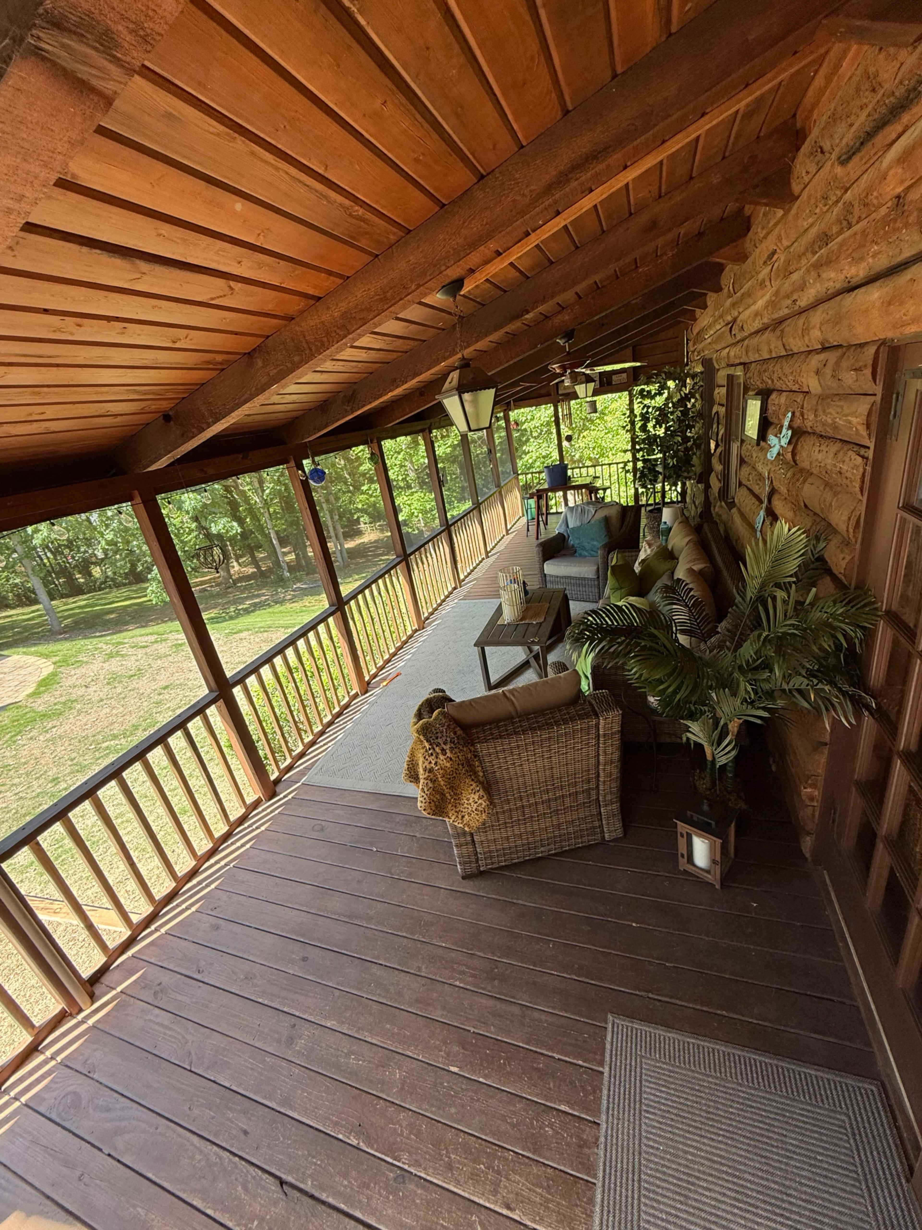 The image shows a rustic porch with wooden paneling, wicker furniture, and a view of greenery outside.