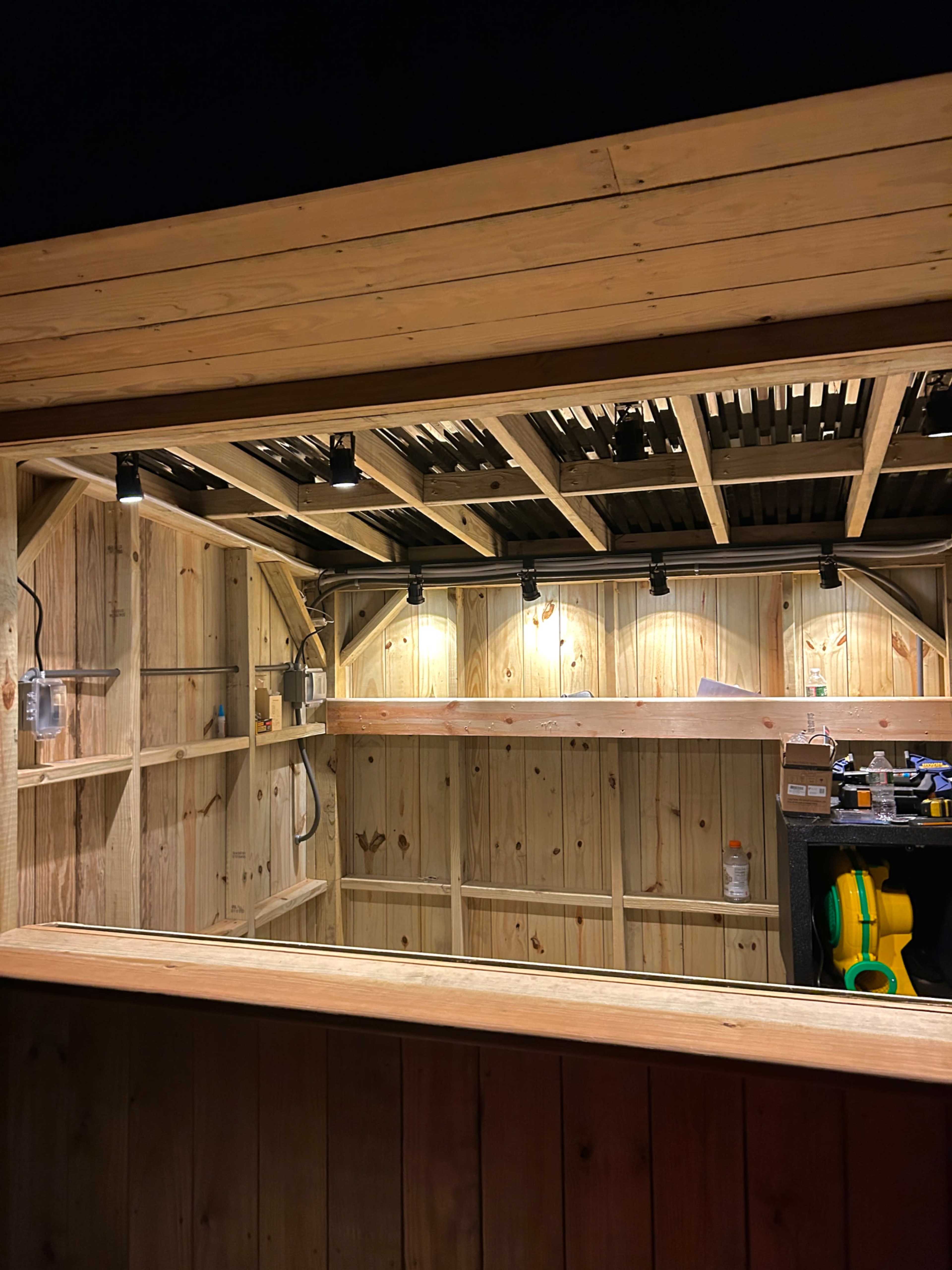 The image shows a wooden structure with shelves and lights inside, likely a shed or storage unit, illuminated in low light.