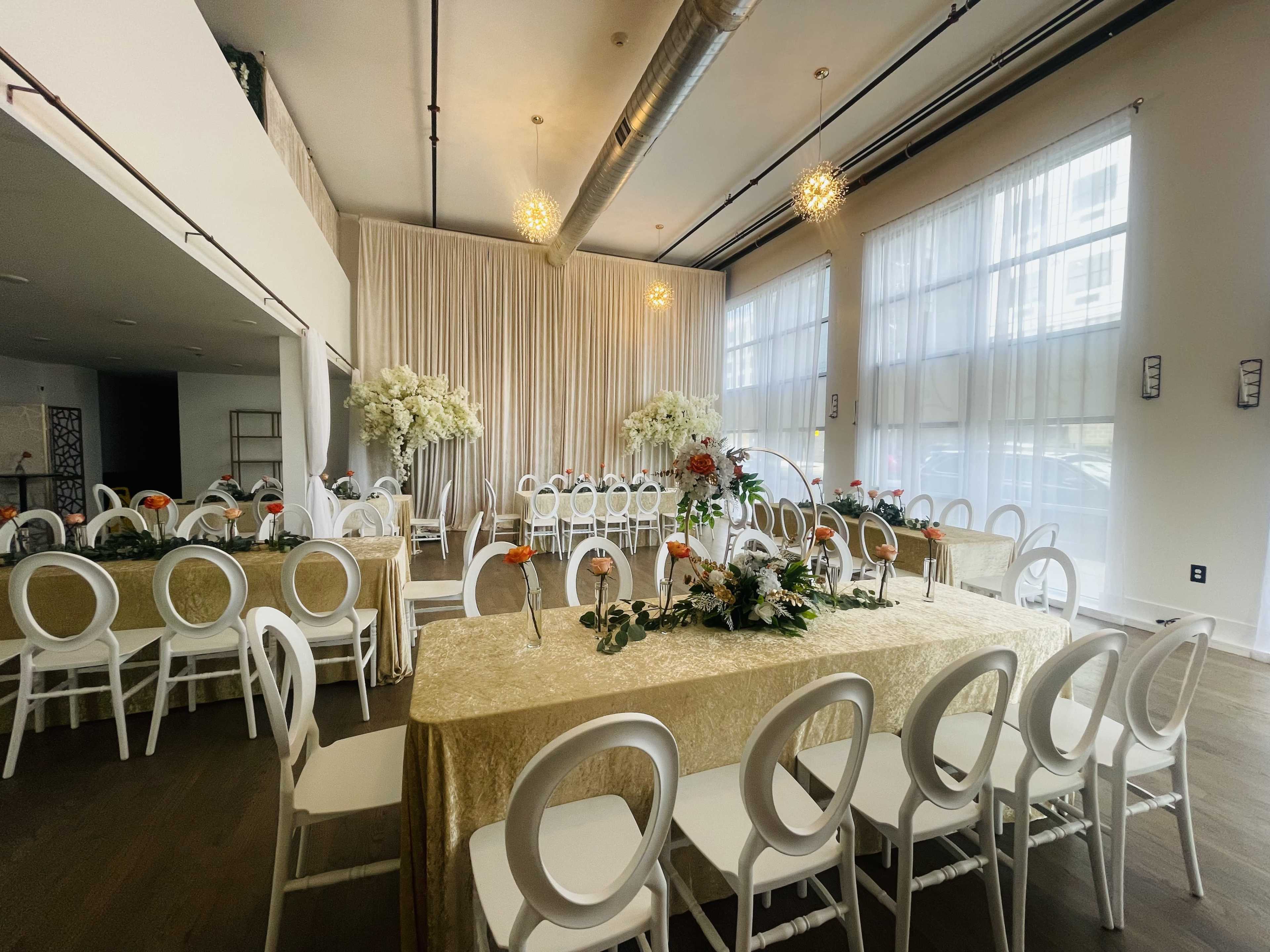 A banquet hall set for an event, featuring elegantly decorated tables with floral arrangements and white chairs arranged in rows.