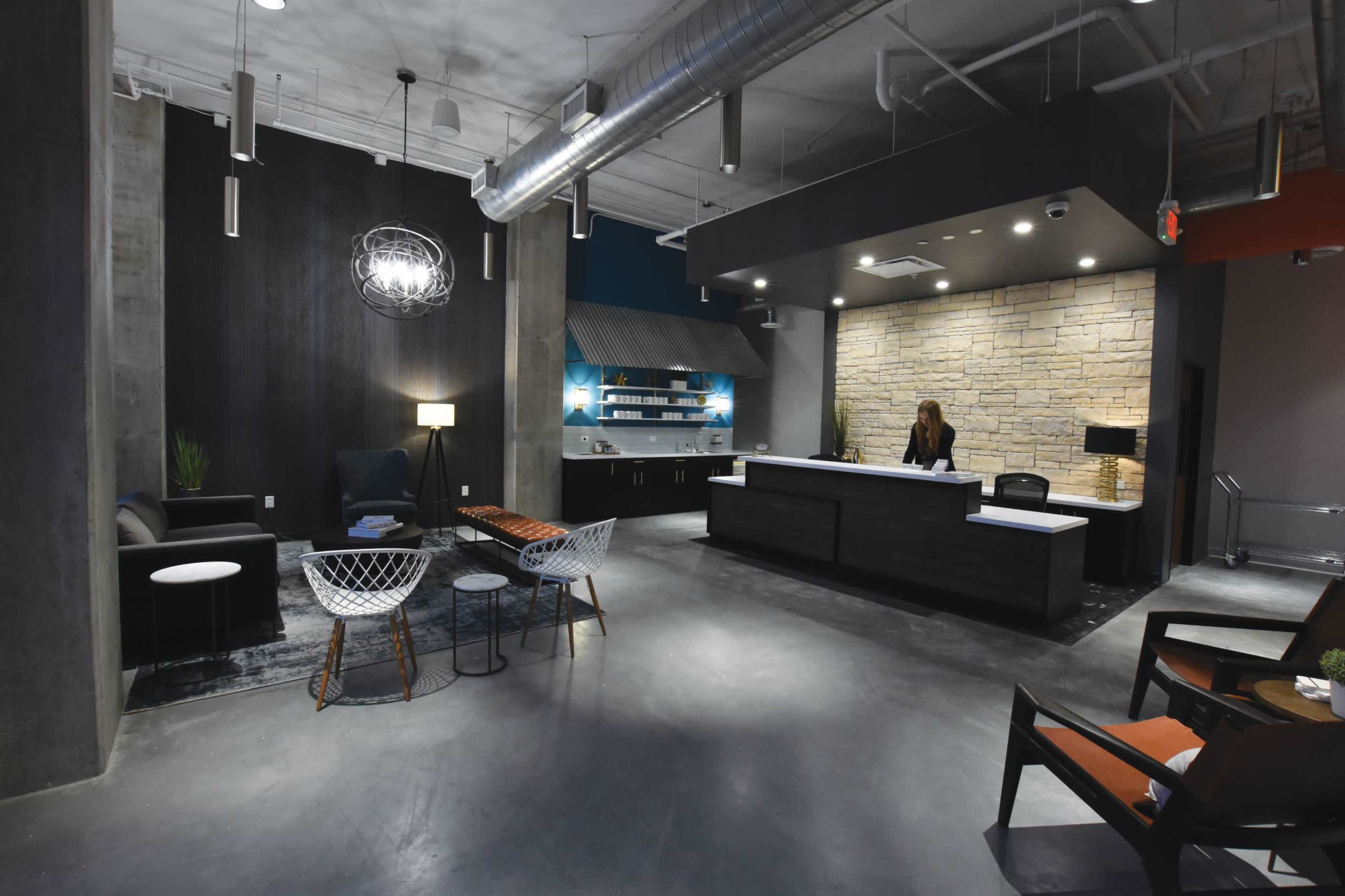 A modern reception area featuring a front desk, seating arrangements, and decorative lighting in a spacious room with concrete flooring.