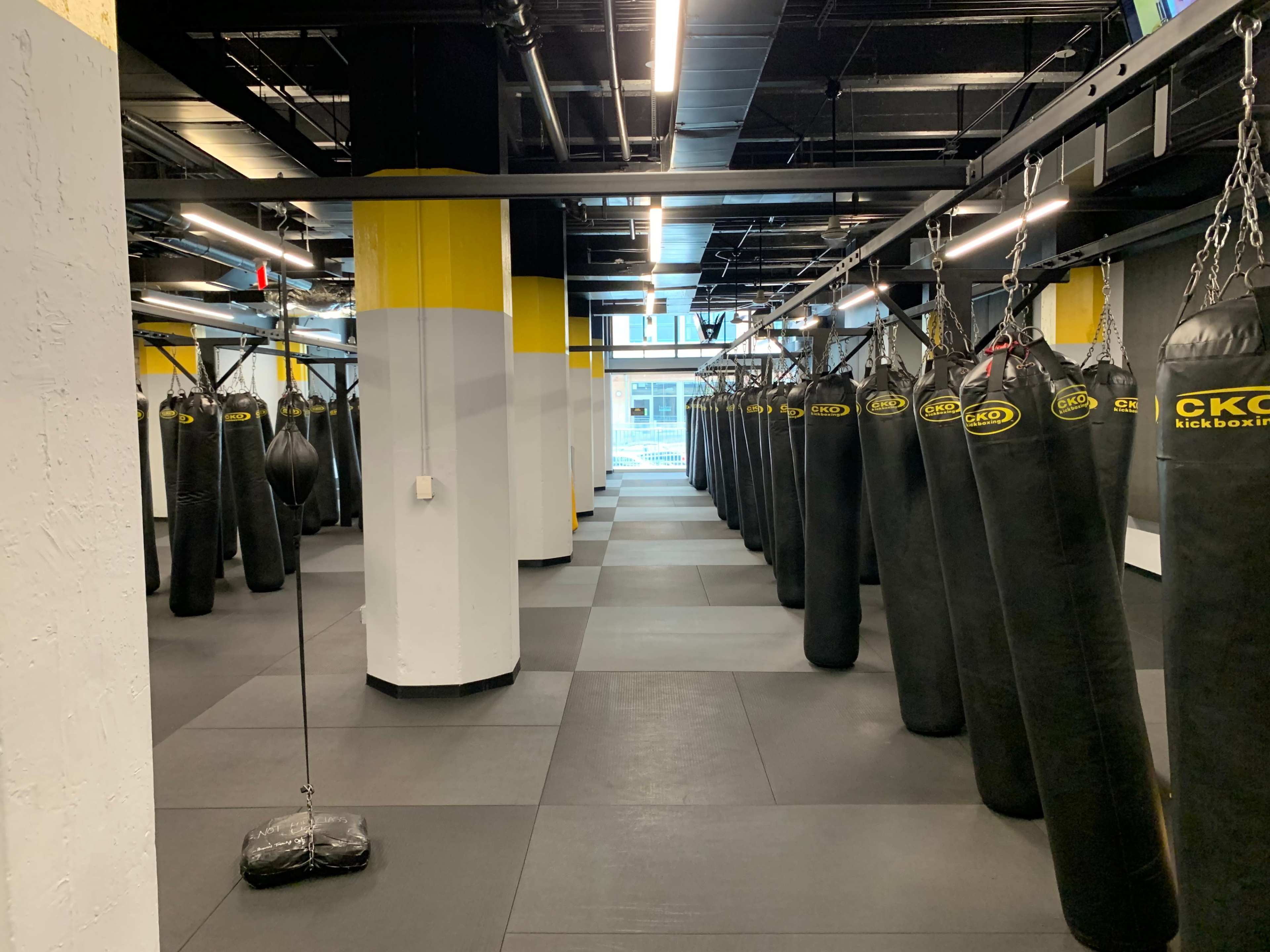 A large, well-lit kickboxing studio filled with hanging black punching bags and equipped with a rubberized floor.
