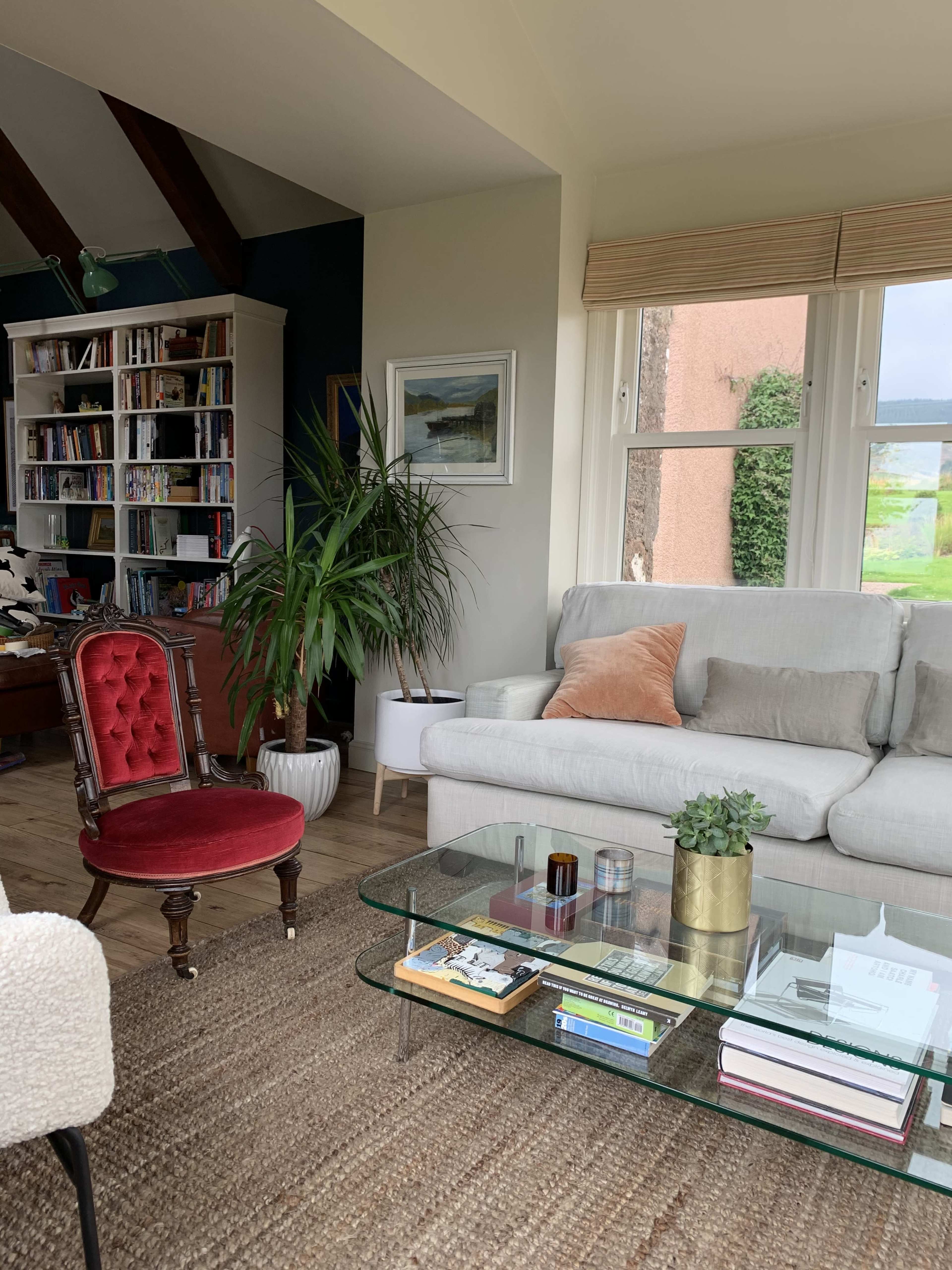 The living room features a gray sofa, a red accent chair, a glass coffee table with various items, and a bookshelf filled with books.
